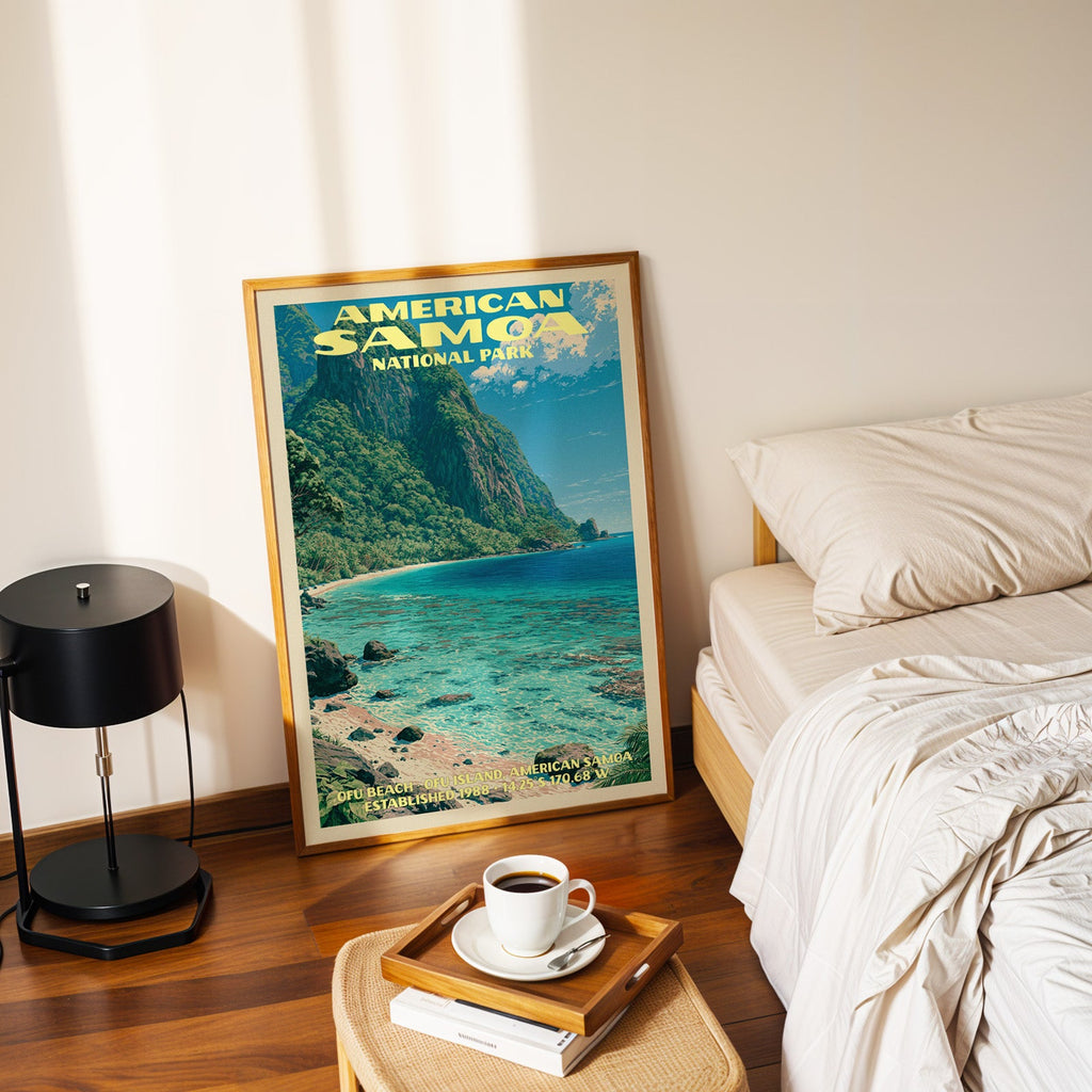 Ofu Beach American Samoa poster in a gold frame on the floor beside a made bed and a black table lamp