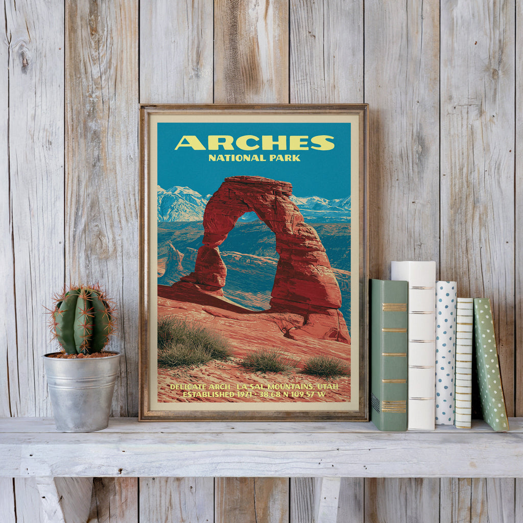 Arches vintage poster in a slim gold frame on a whitewashed plank wall beside a cactus and pastel books