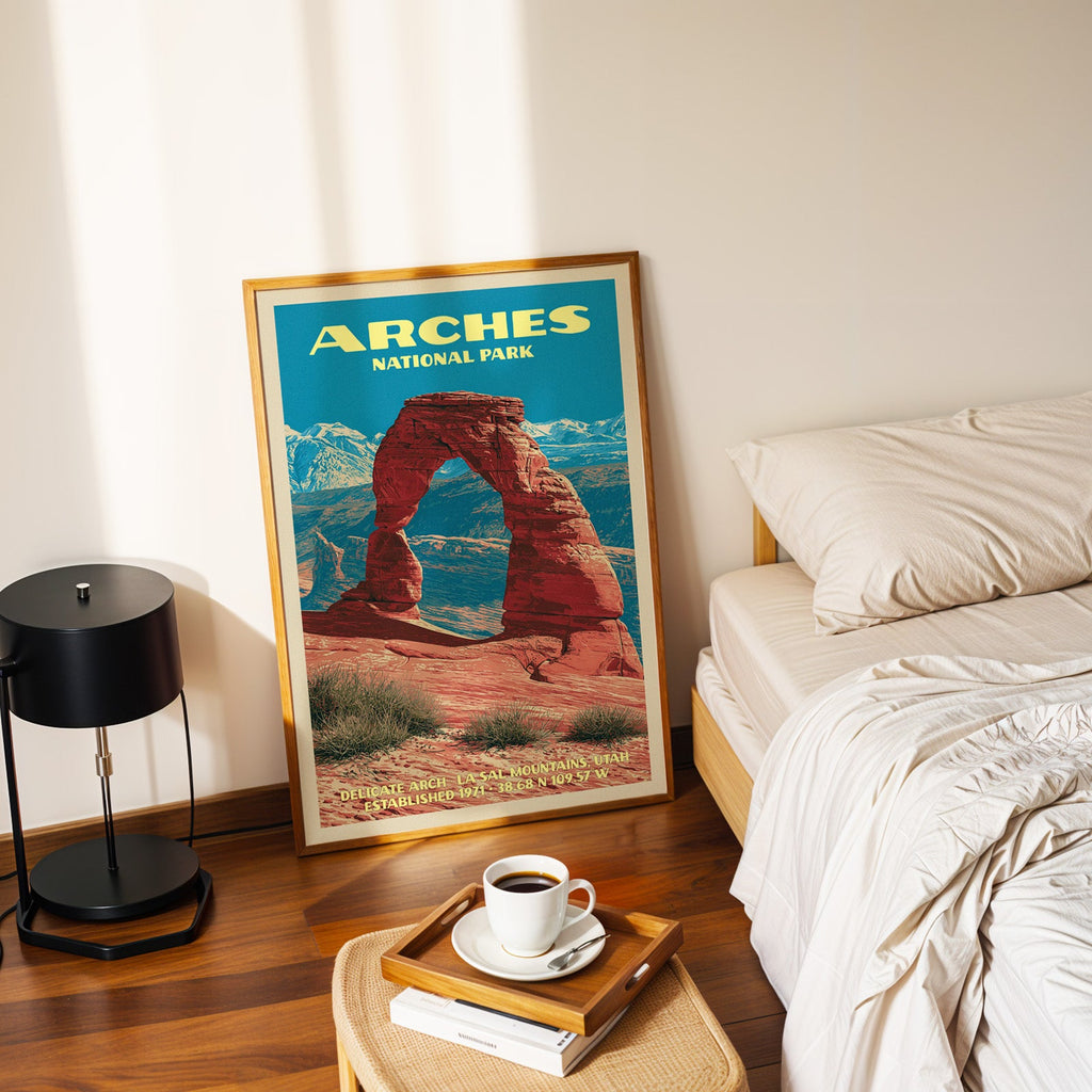 Delicate Arch Arches poster in a gold frame on the floor beside a made bed and a black table lamp