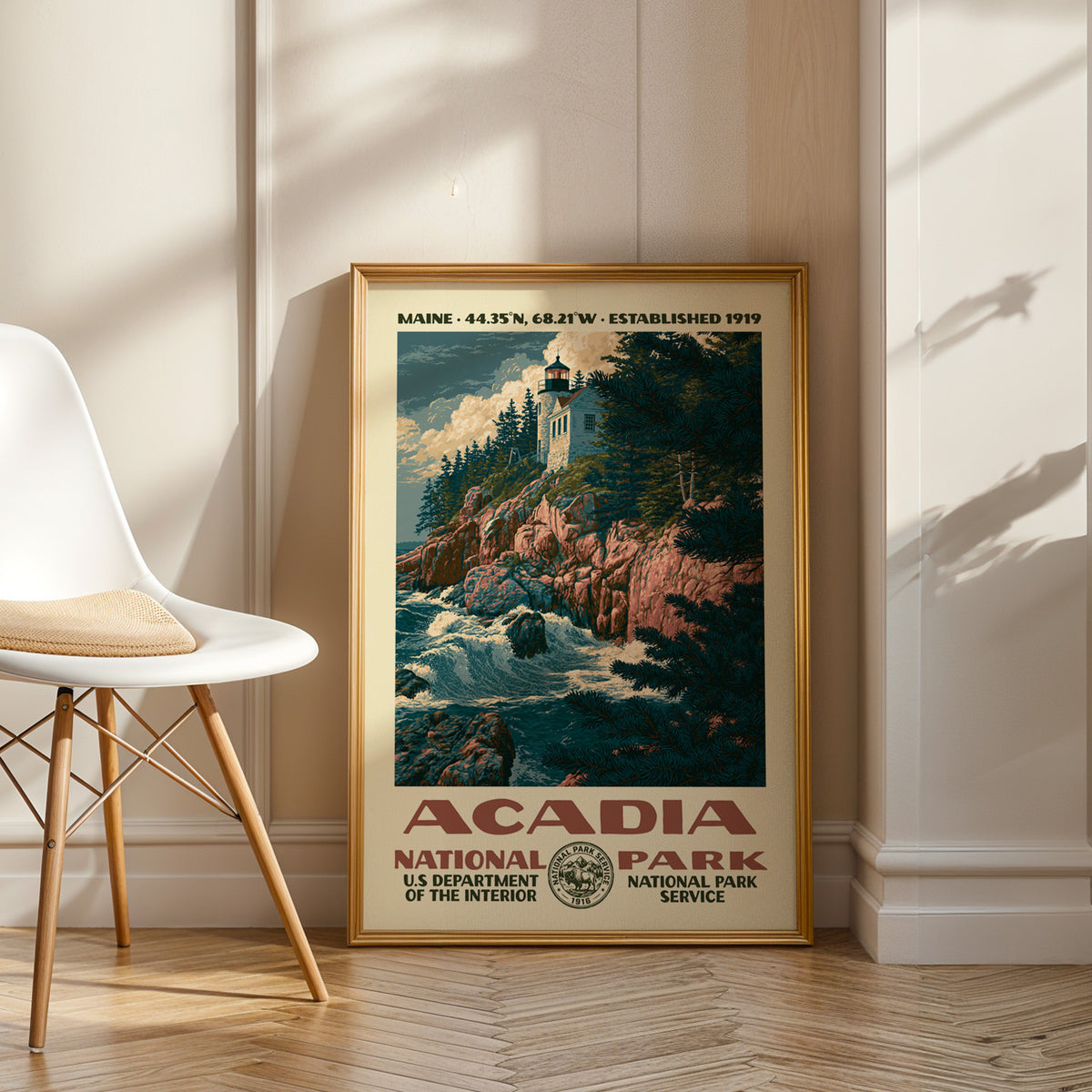 Acadia National Park vintage WPA art in an oak frame leaning by a white chair on a wood floor