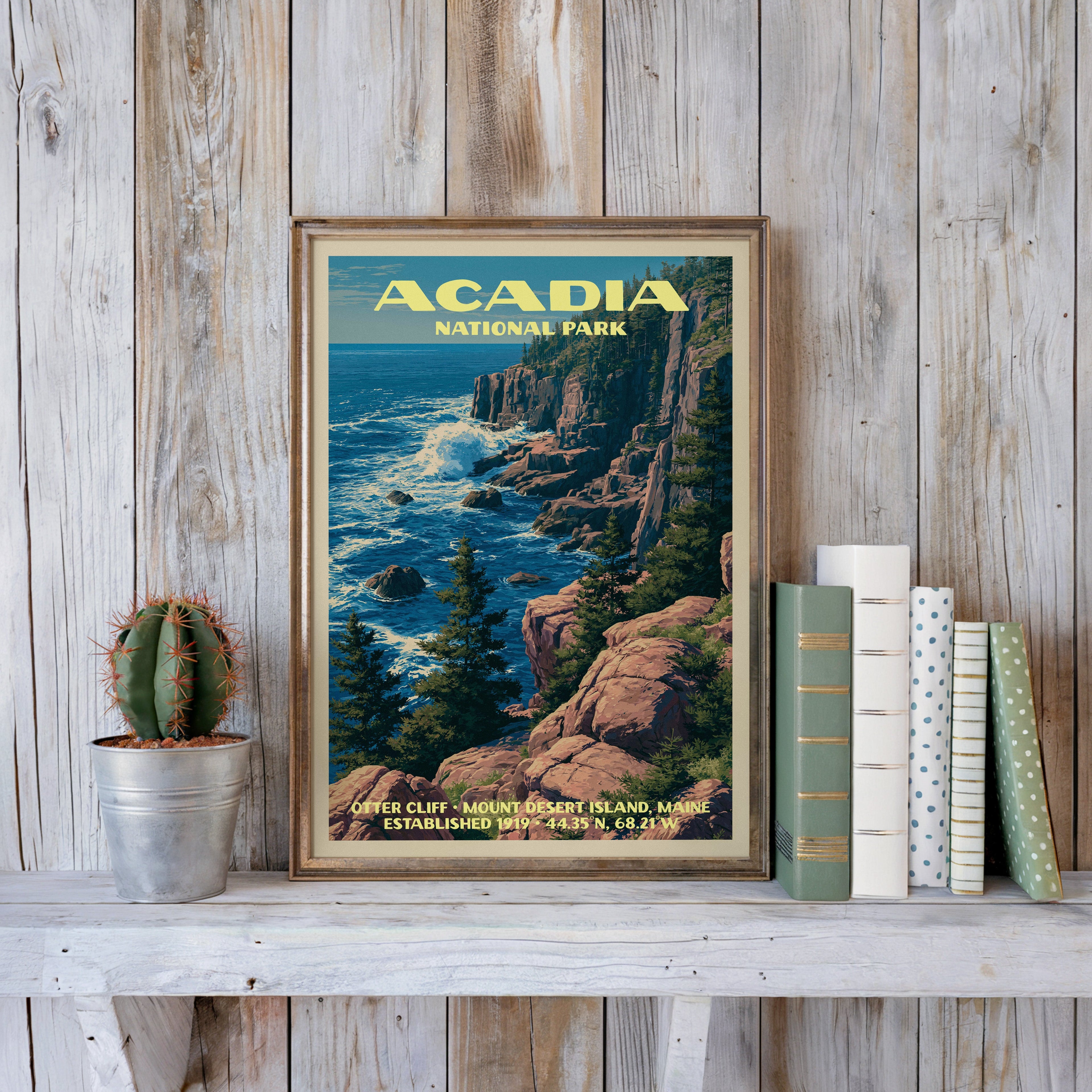 Acadia vintage poster in a slim gold frame on a whitewashed plank wall beside a cactus and pastel books
