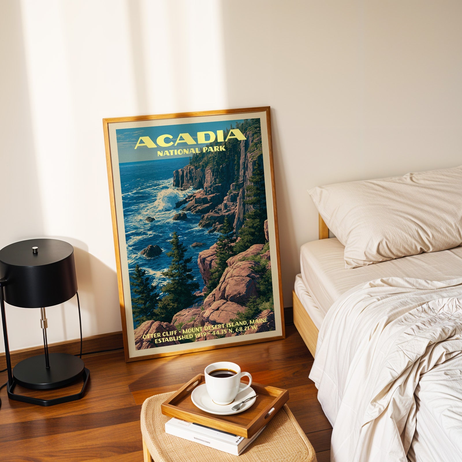 Acadia Otter Cliff poster in a gold frame on the floor beside a made bed and a black table lamp
