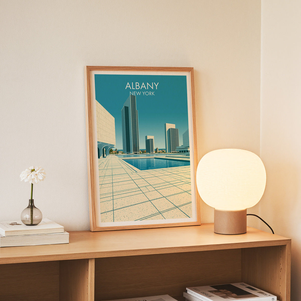Reflecting pool print in a slim oak frame standing on an oak console beside white daisies in a glass jar.