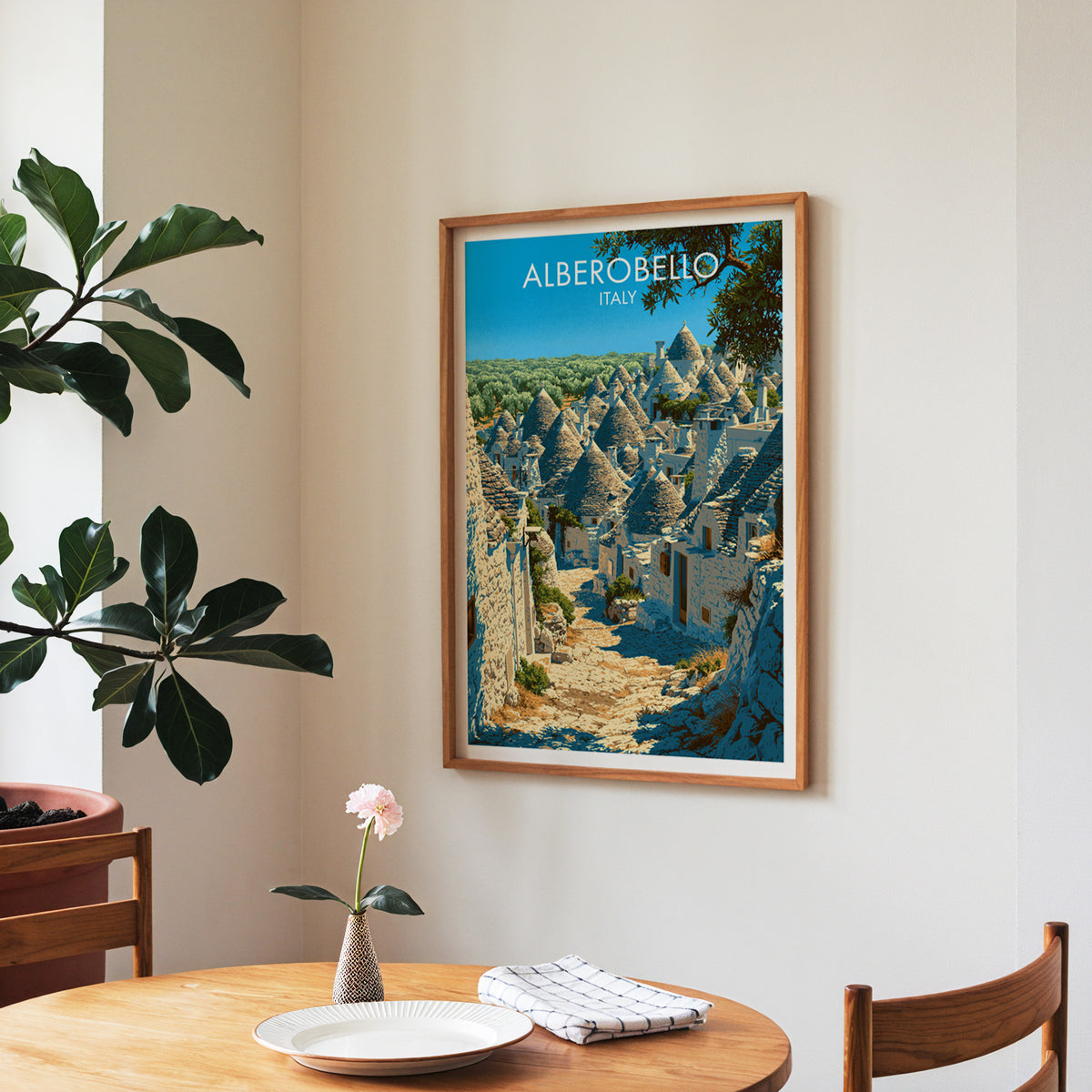 Alberobello poster, walnut frame in a dining corner above a round table and a fiddle-leaf fig