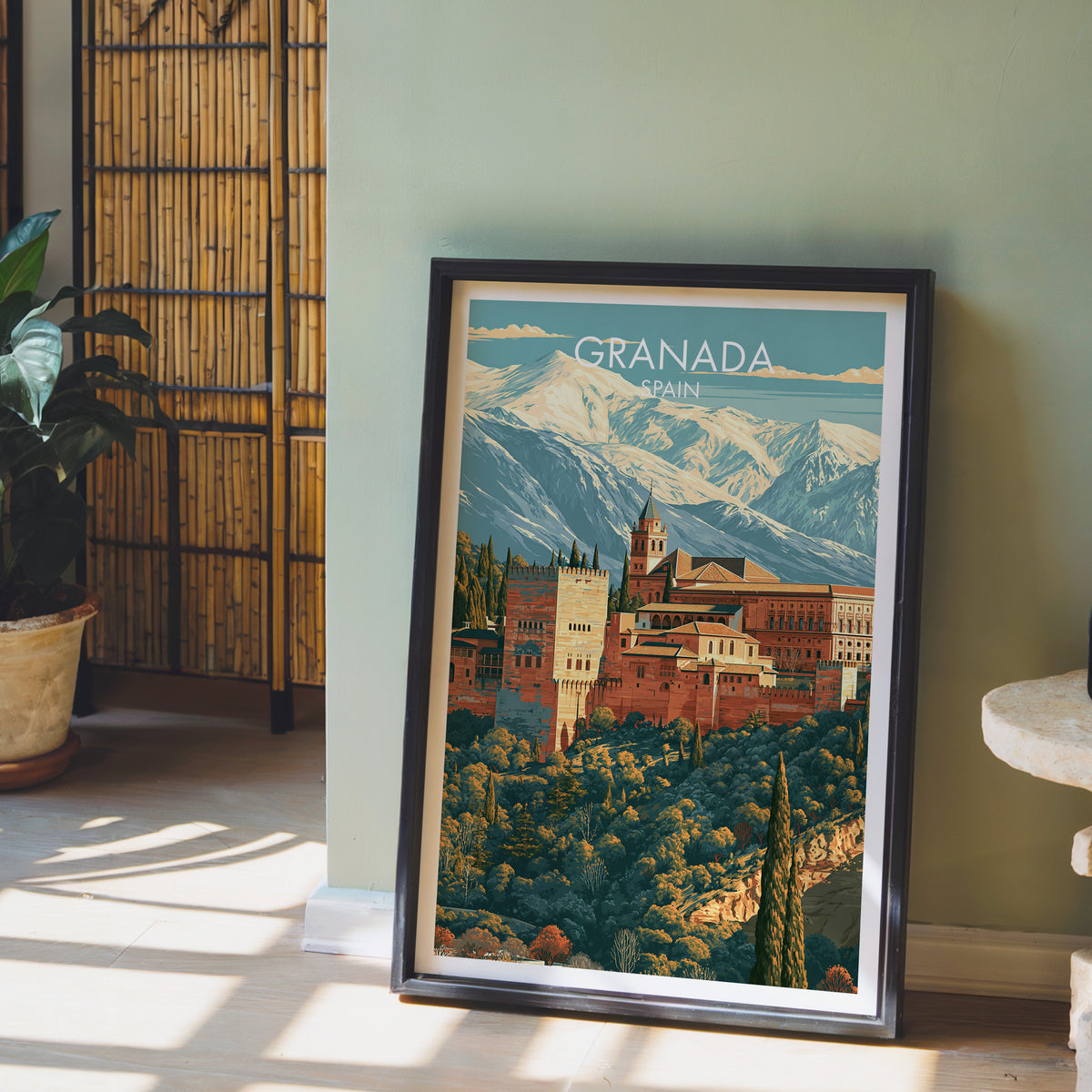 Alhambra Granada poster leaning on a sage green wall beside a bamboo screen and a potted plant in afternoon sun