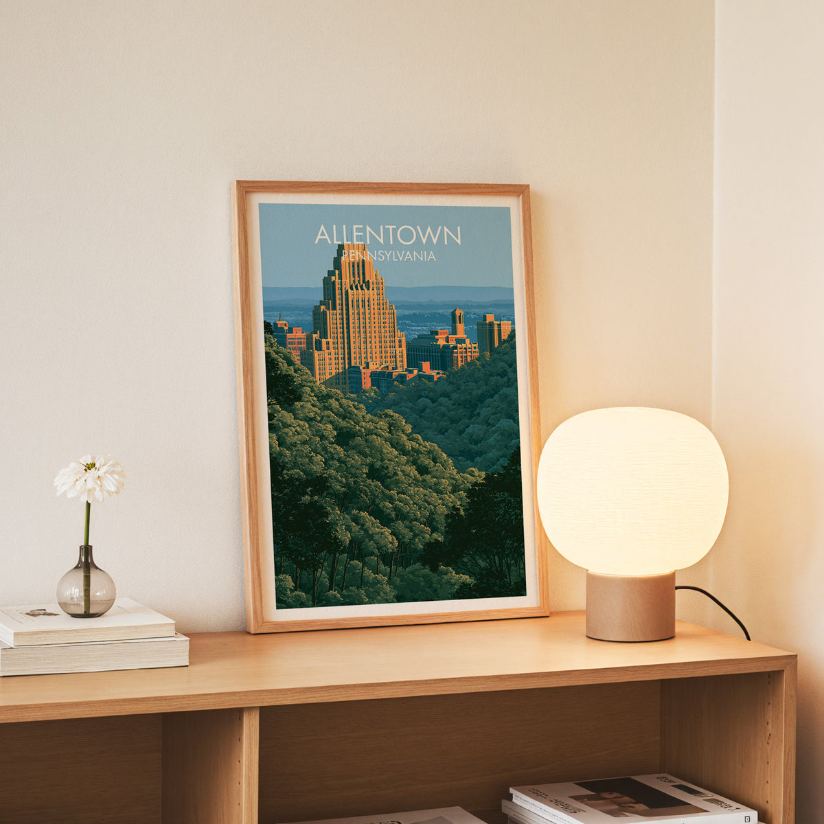 Wooded ridge skyline print in a slim oak frame on an oak console beside white daisies in a glass jar.