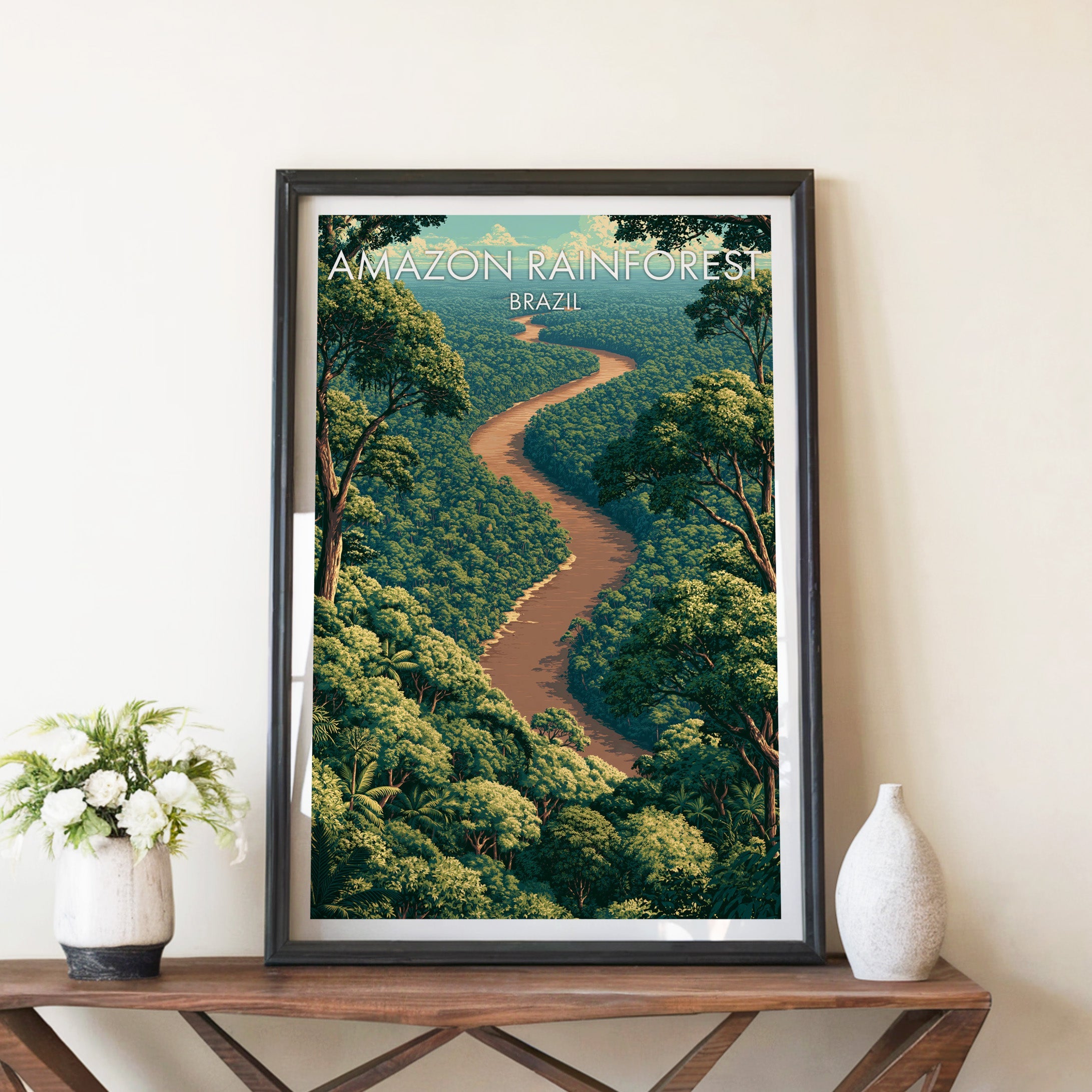 Amazon River print in a black frame on a brown console table with white flowers in a ceramic vase