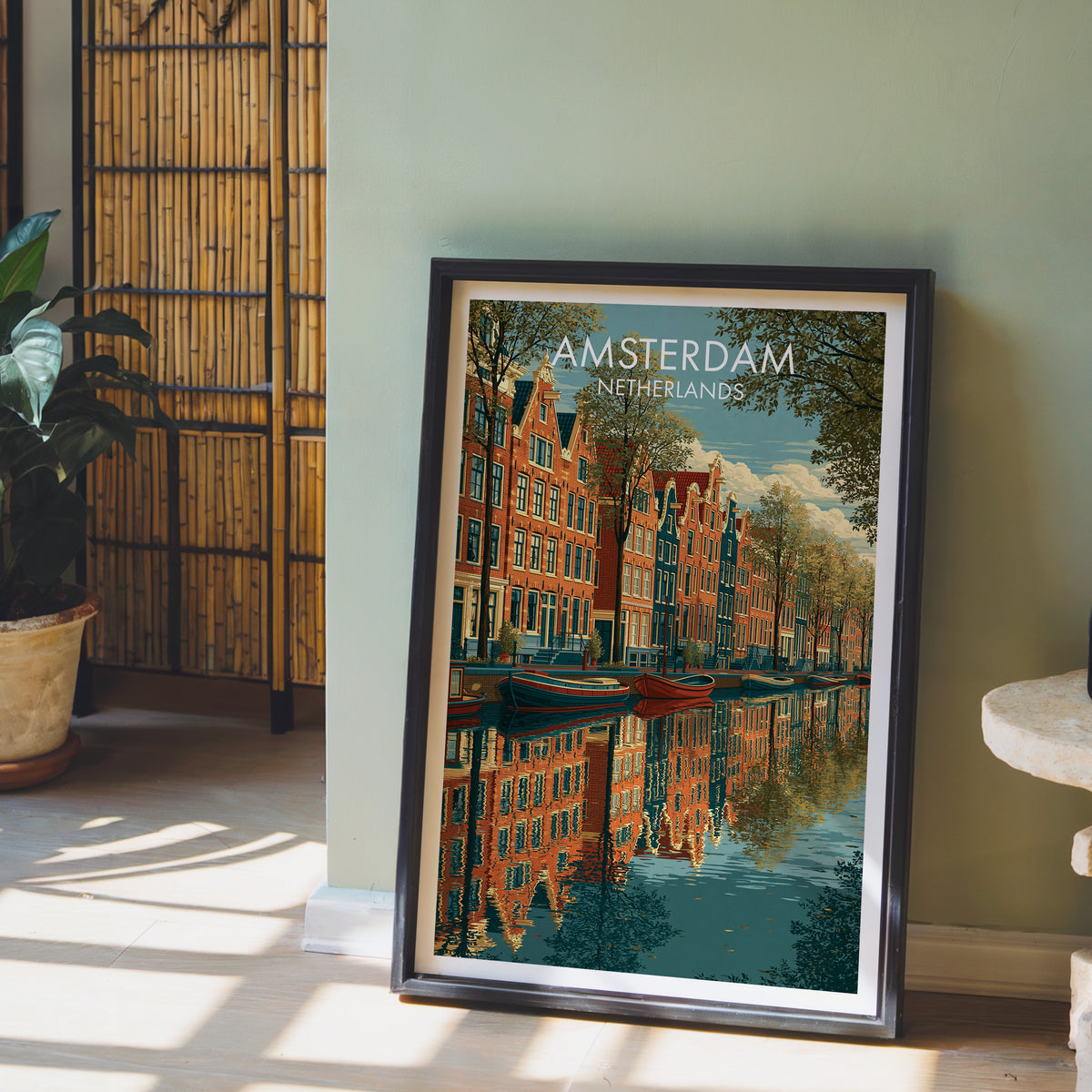 Amsterdam canal poster leaning on a sage green wall beside a bamboo screen and a potted plant in afternoon sun