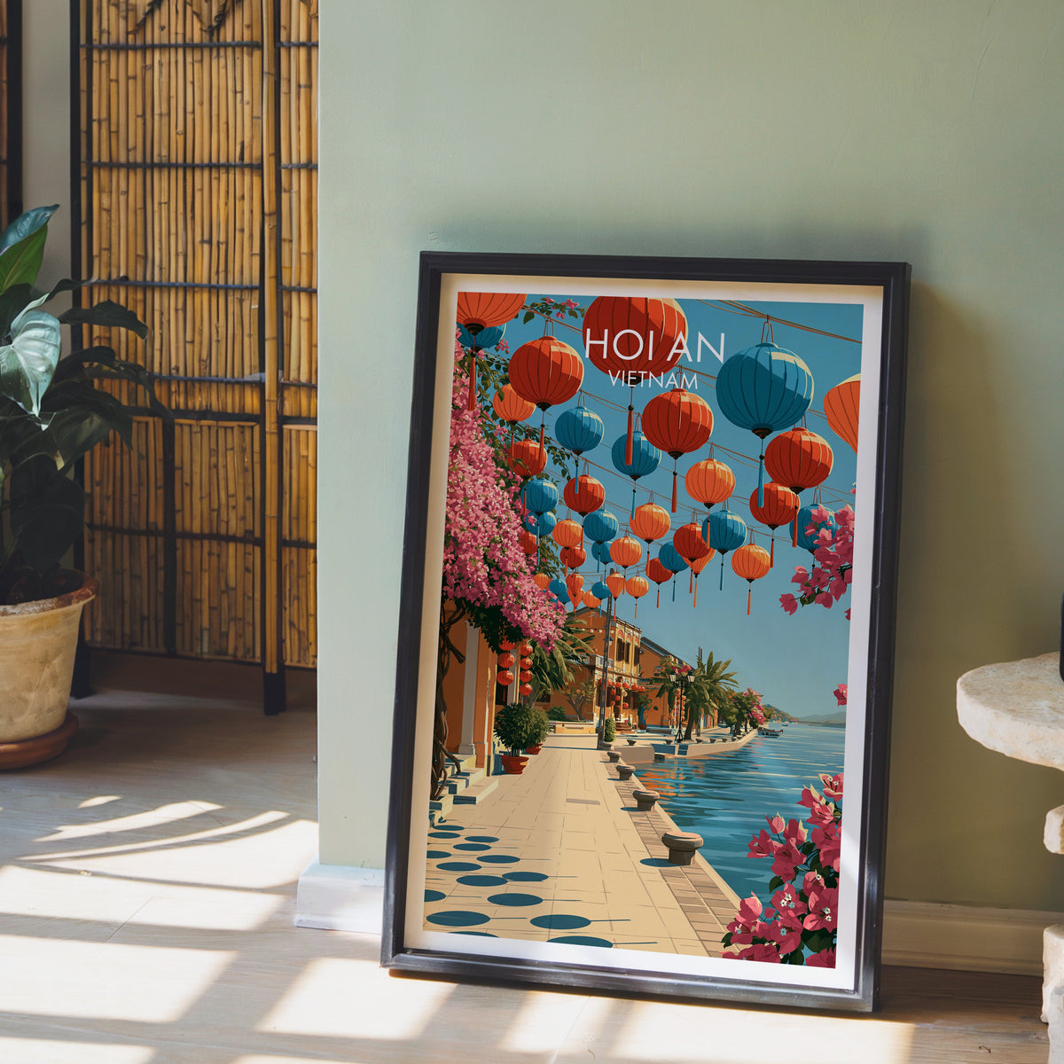Hoi An travel print in a black frame leaning against a sage green wall beside a bamboo screen