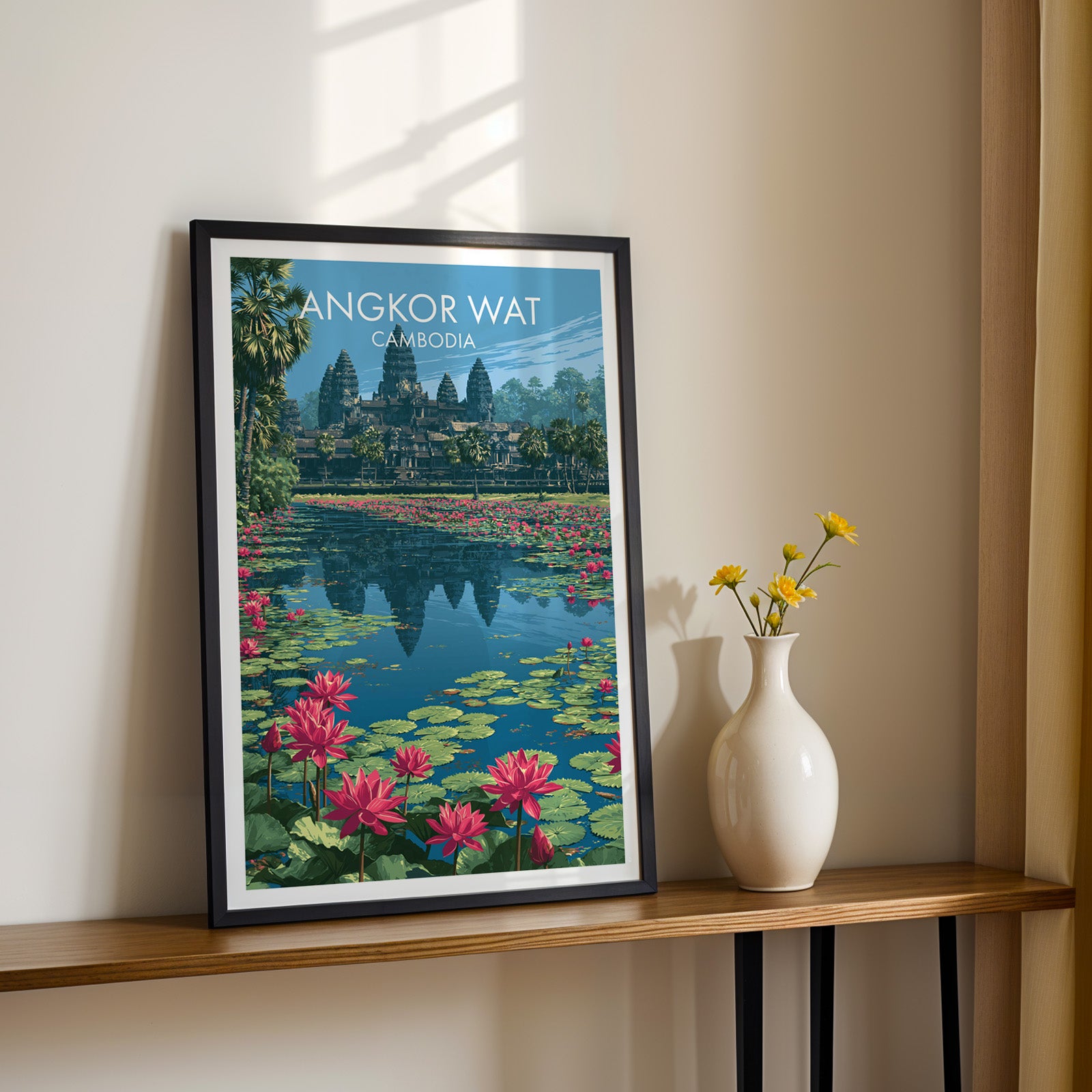 Black framed Angkor Wat Cambodia print on a narrow hallway console in sunlight, styled with yellow flowers