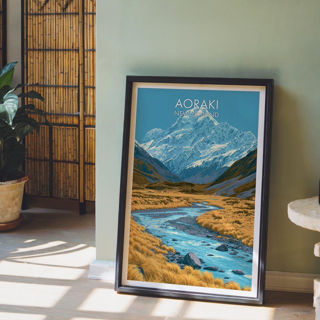 New Zealand mountain print in a black frame on a pale wood floor by a sage-green wall and bamboo screen
