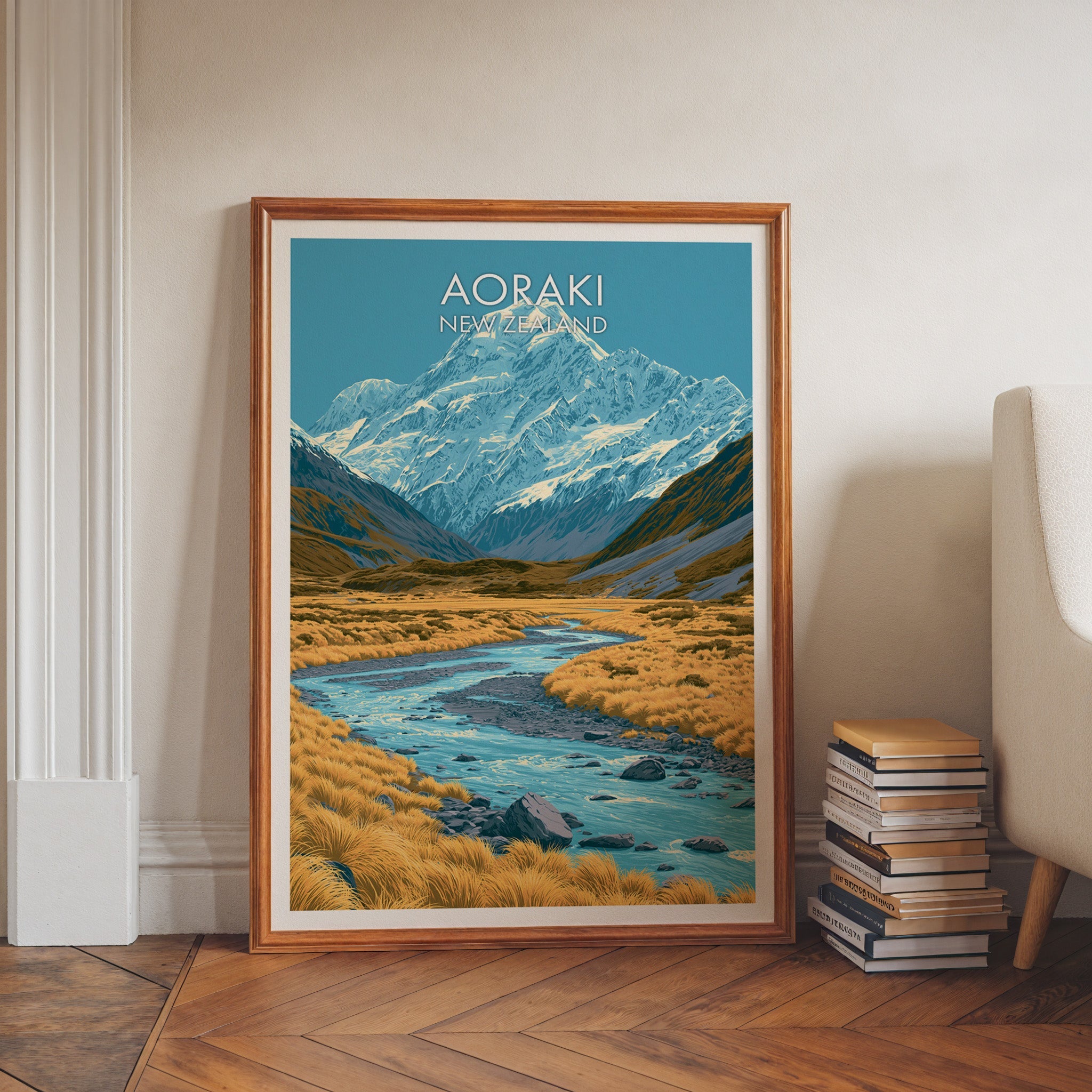 Aoraki artwork in a walnut frame on herringbone floor beside stacked books and a pale armchair
