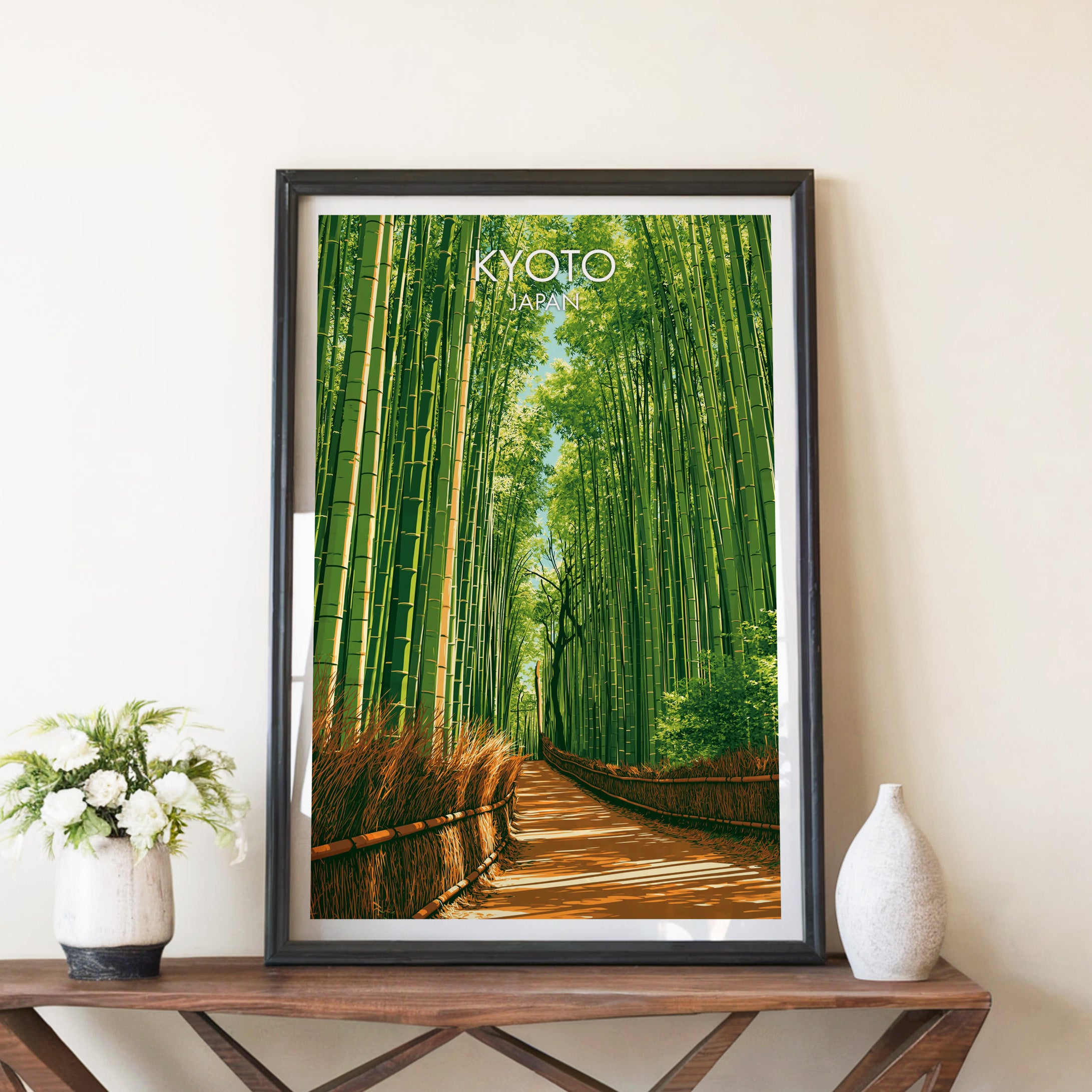 Arashiyama Bamboo Forest Kyoto travel poster in a black frame on a wooden console table with white flowers