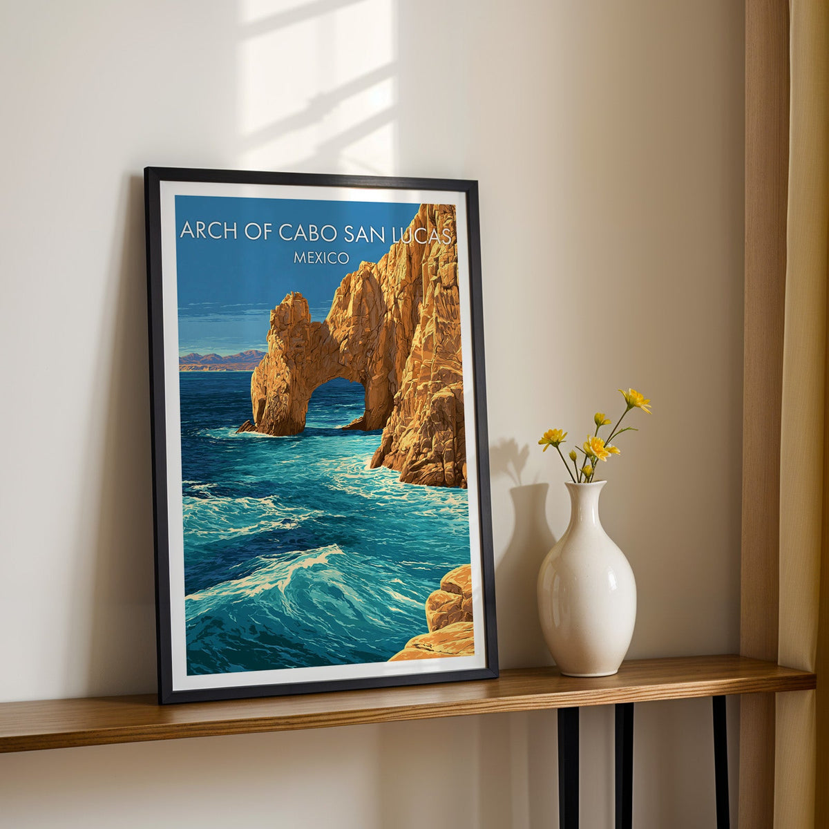 Turquoise surf and amber cliffs, black frame on a wood shelf with yellow daisies on a cream wall