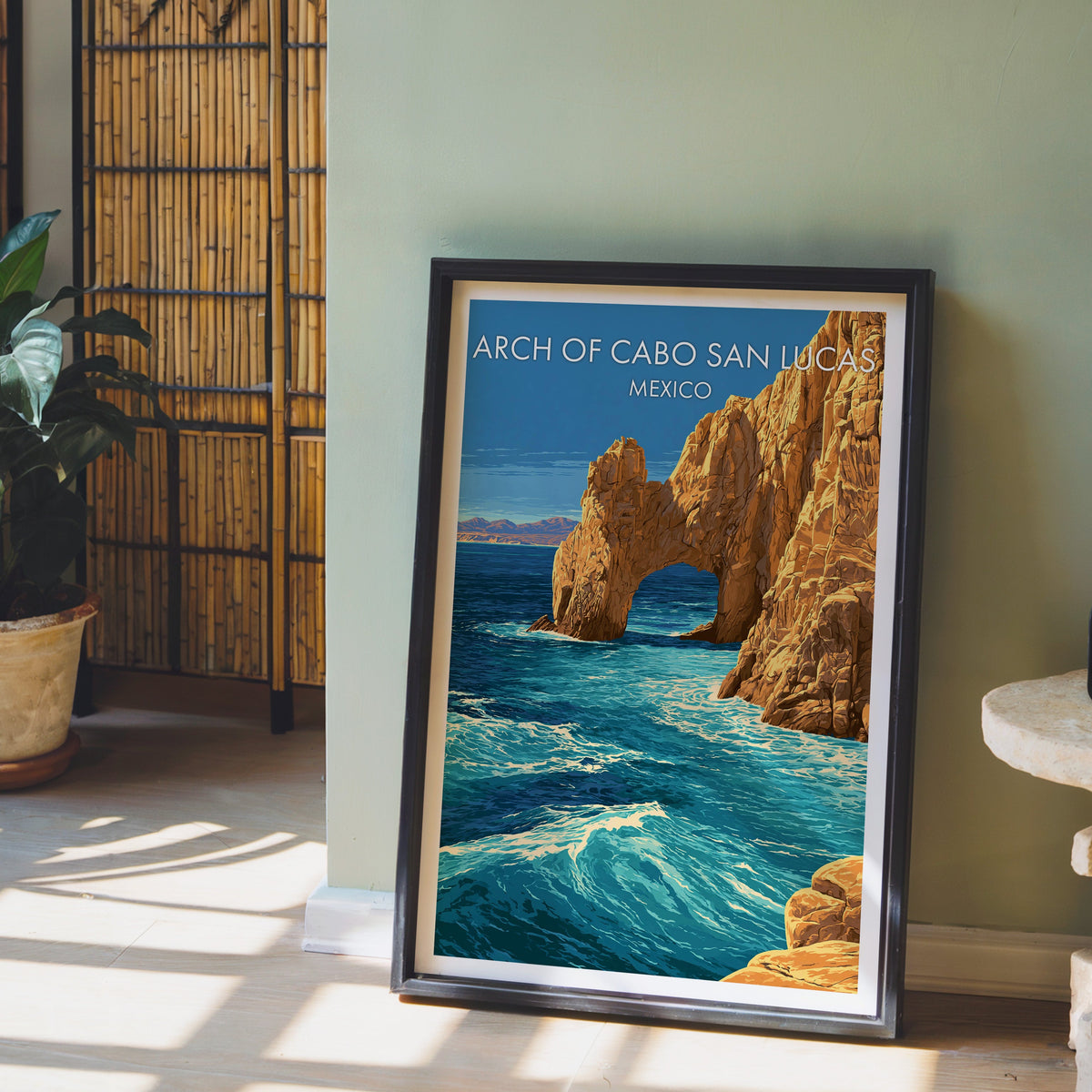 Rock arch over the sea, black frame leaning on pale wood floor by a sage wall and bamboo screen