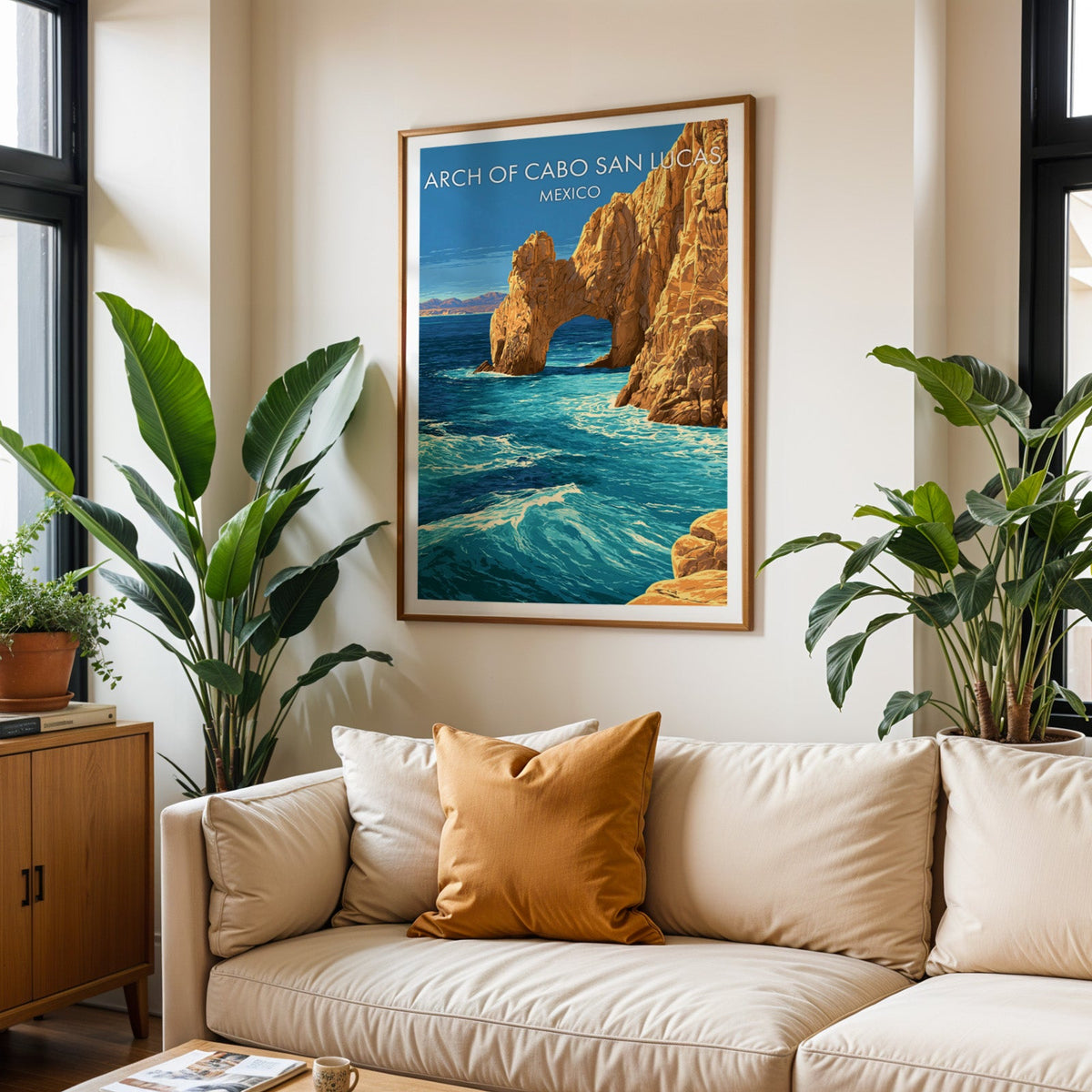 Cabo San Lucas travel print in an oak frame above a cream sofa with a burnt-orange cushion and plants