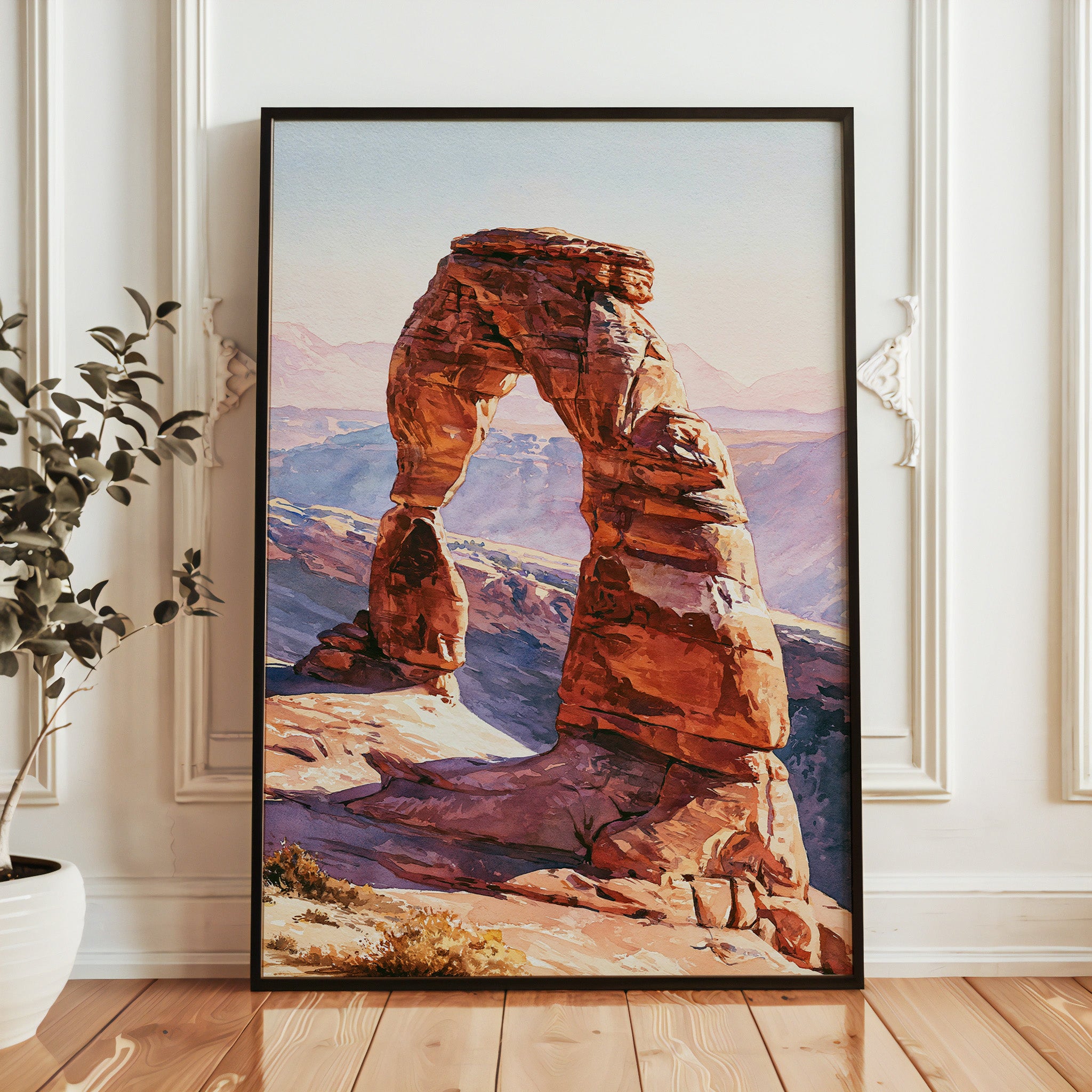 Framed artwork of a desert arch on a wall in a room with a plant.