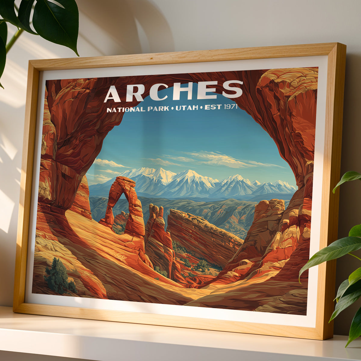 Arches National Park wall art print in a light oak frame, leaning on a white shelf in warm sunlight beside a monstera plant