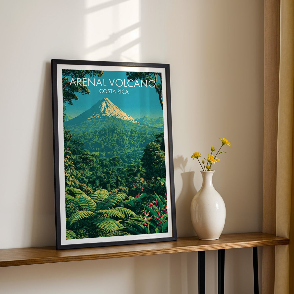 Costa Rica rainforest scene in a black frame on a narrow wood shelf, yellow daisies on a sunlit cream wall