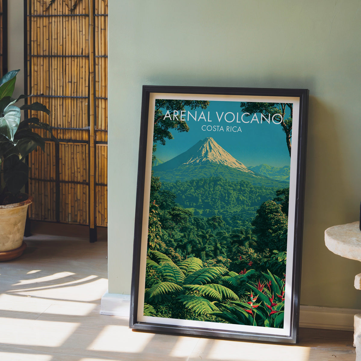 Tree ferns below a volcano, black frame leaning on pale wood floor by a sage wall and a bamboo screen