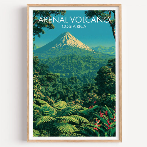 Arenal Volcano travel print in a light oak frame on a plain white wall, sunlit cone above green rainforest