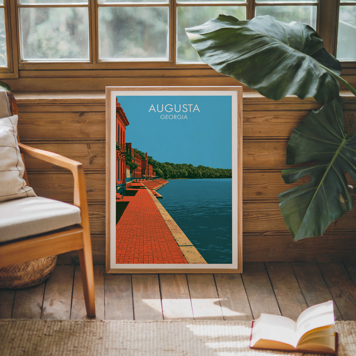 Savannah River print in an oak frame on sun-washed wood panelling near a mid-century armchair and open book.