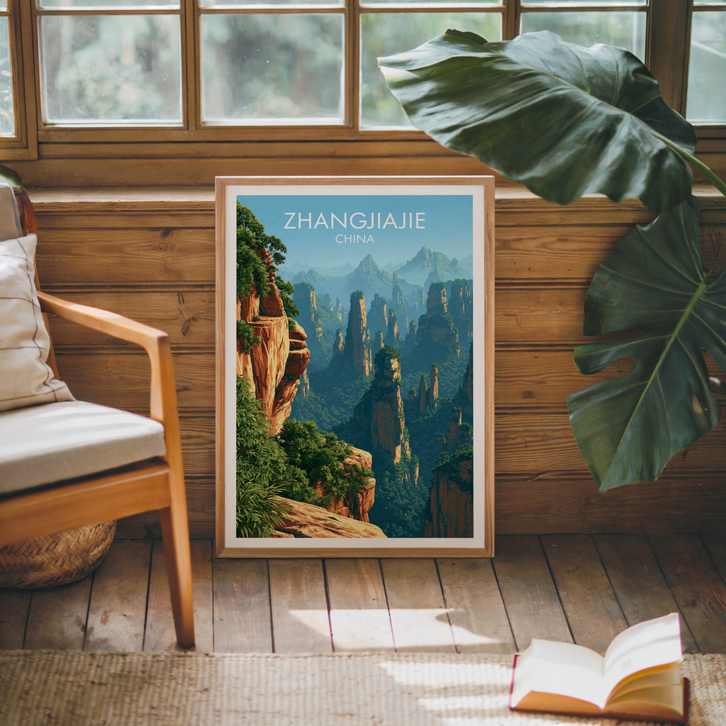 Framed Zhangjiajie China poster leaning against a timber cabin wall with monstera leaves and an open book