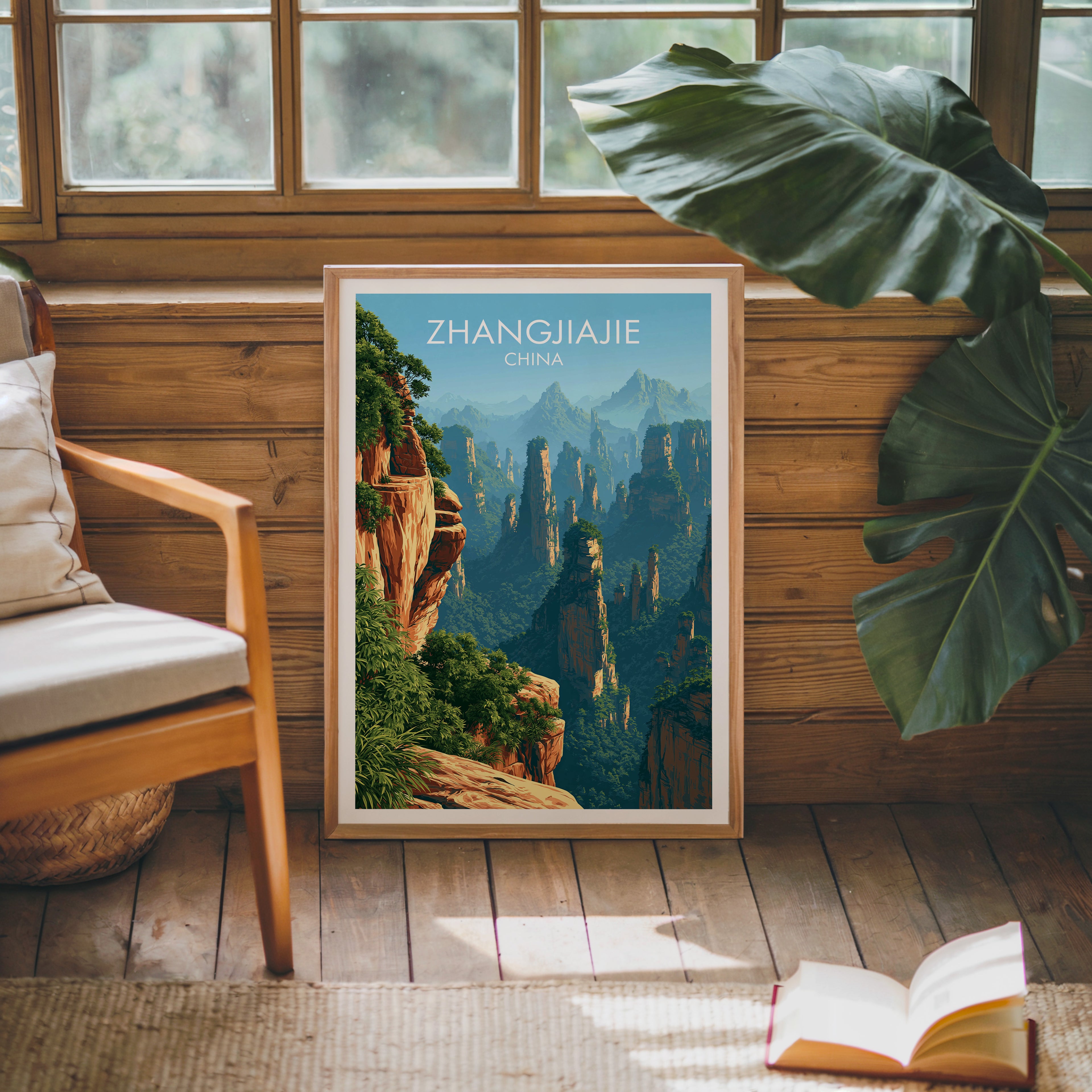 Framed Zhangjiajie China poster leaning against a timber cabin wall with monstera leaves and an open book