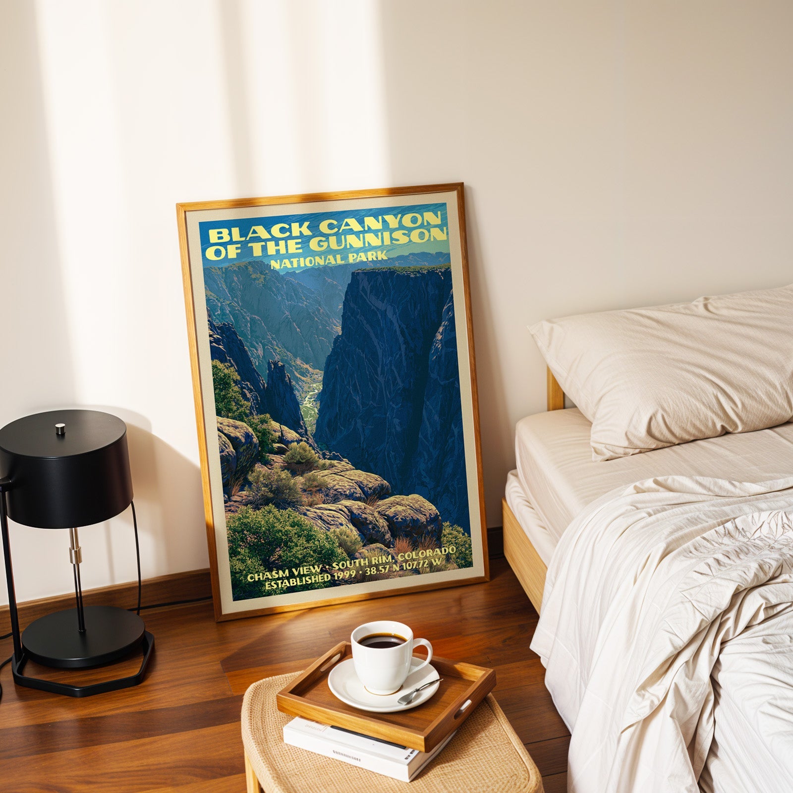 Chasm View Black Canyon poster in a gold frame on the floor beside a made bed and a black table lamp