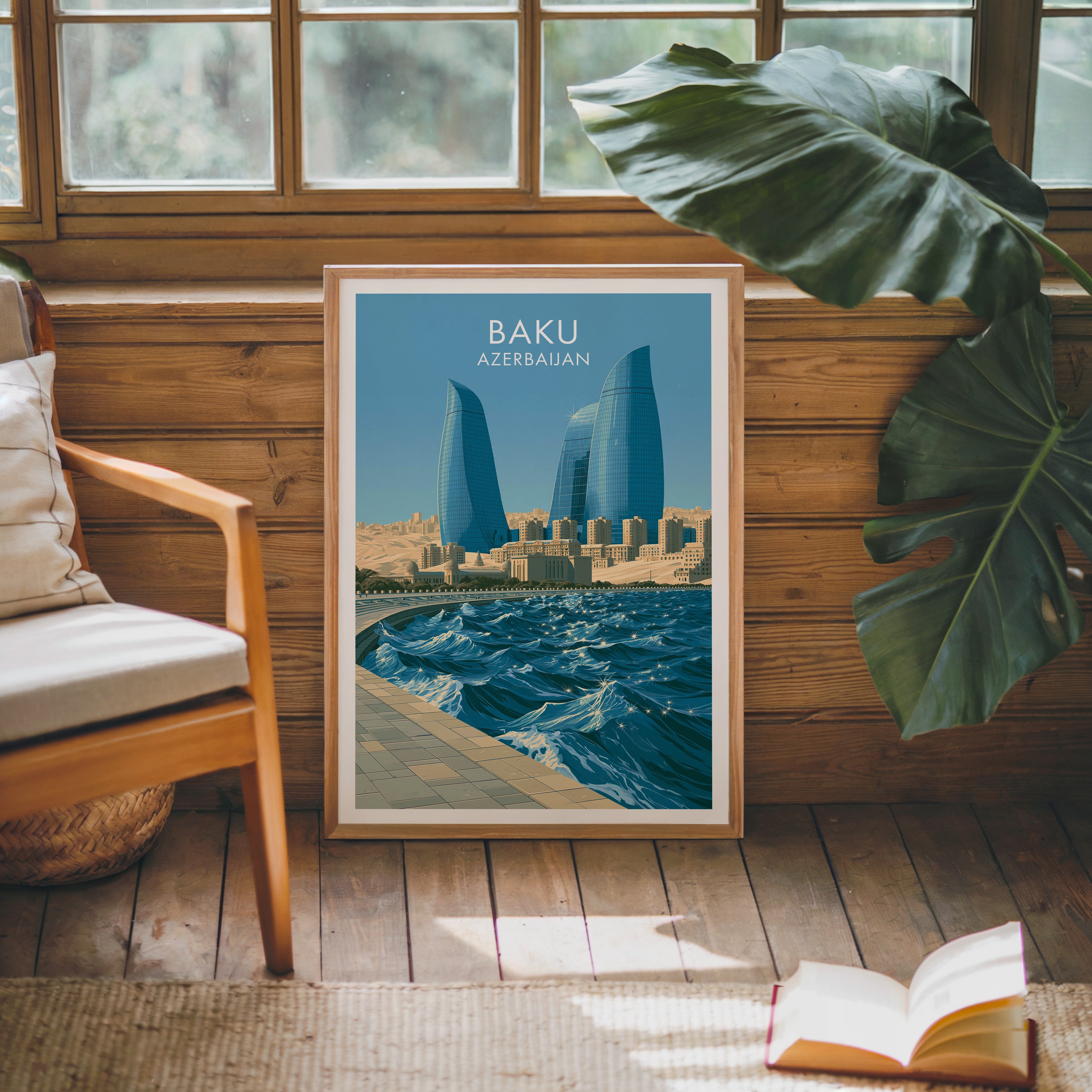 Framed Baku Azerbaijan poster leaning against a timber cabin wall with monstera leaves and an open book