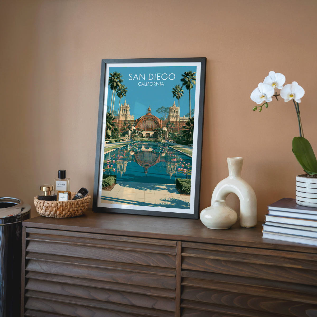 San Diego Lily Pond poster in a black frame on a walnut sideboard, terracotta wall, orchid and rattan tray