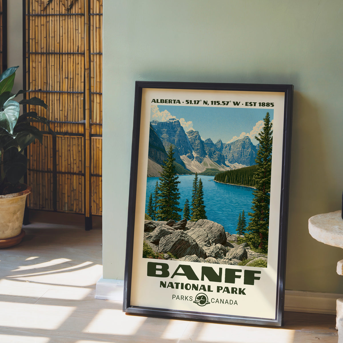 Banff Canada vintage poster in a black frame on the floor by a sage wall and bamboo screen