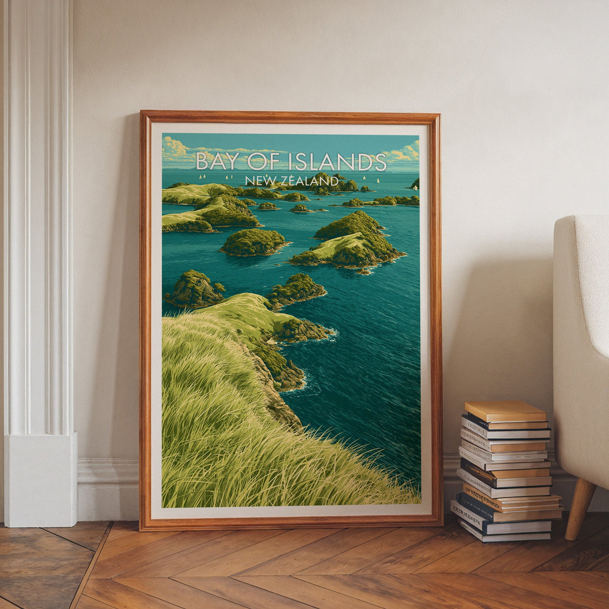 Green island seascape in a walnut frame on a herringbone floor beside stacked books and a pale armchair