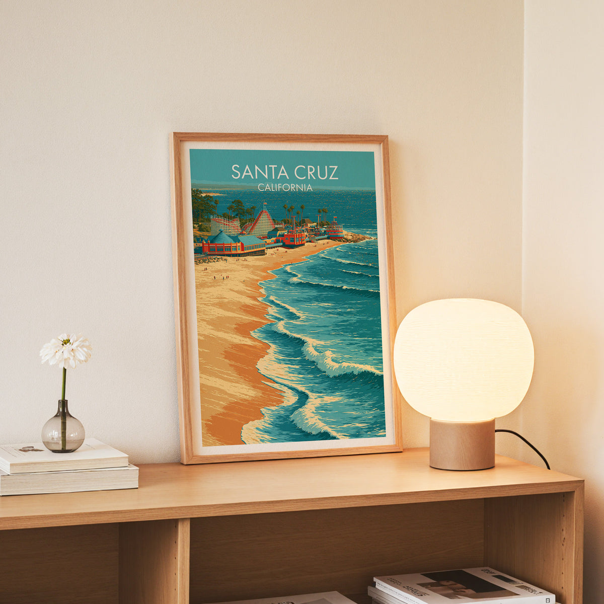 Slim oak framed Santa Cruz boardwalk print on a console beside white daisies in a glass jar
