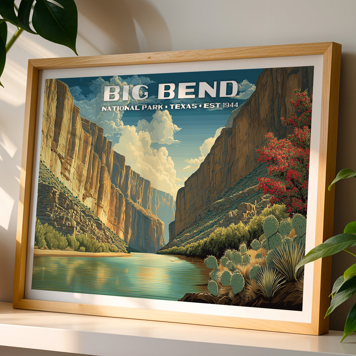 Big Bend National Park wall art print in a light oak frame, leaning on a white shelf in warm sunlight beside a monstera plant