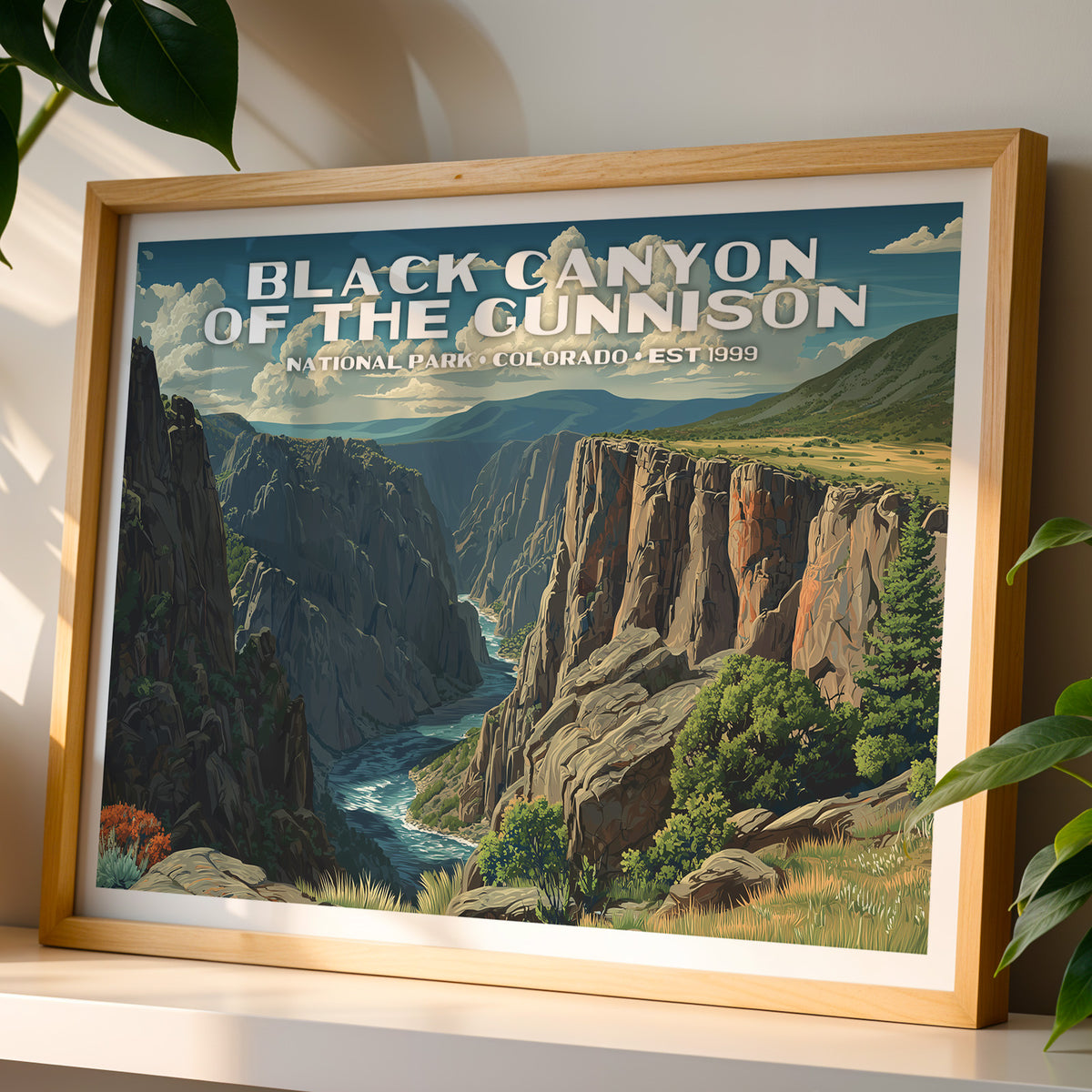 Black Canyon of the Gunnison National Park wall art print in a light oak frame, leaning on a white shelf in warm sunlight beside a monstera plant