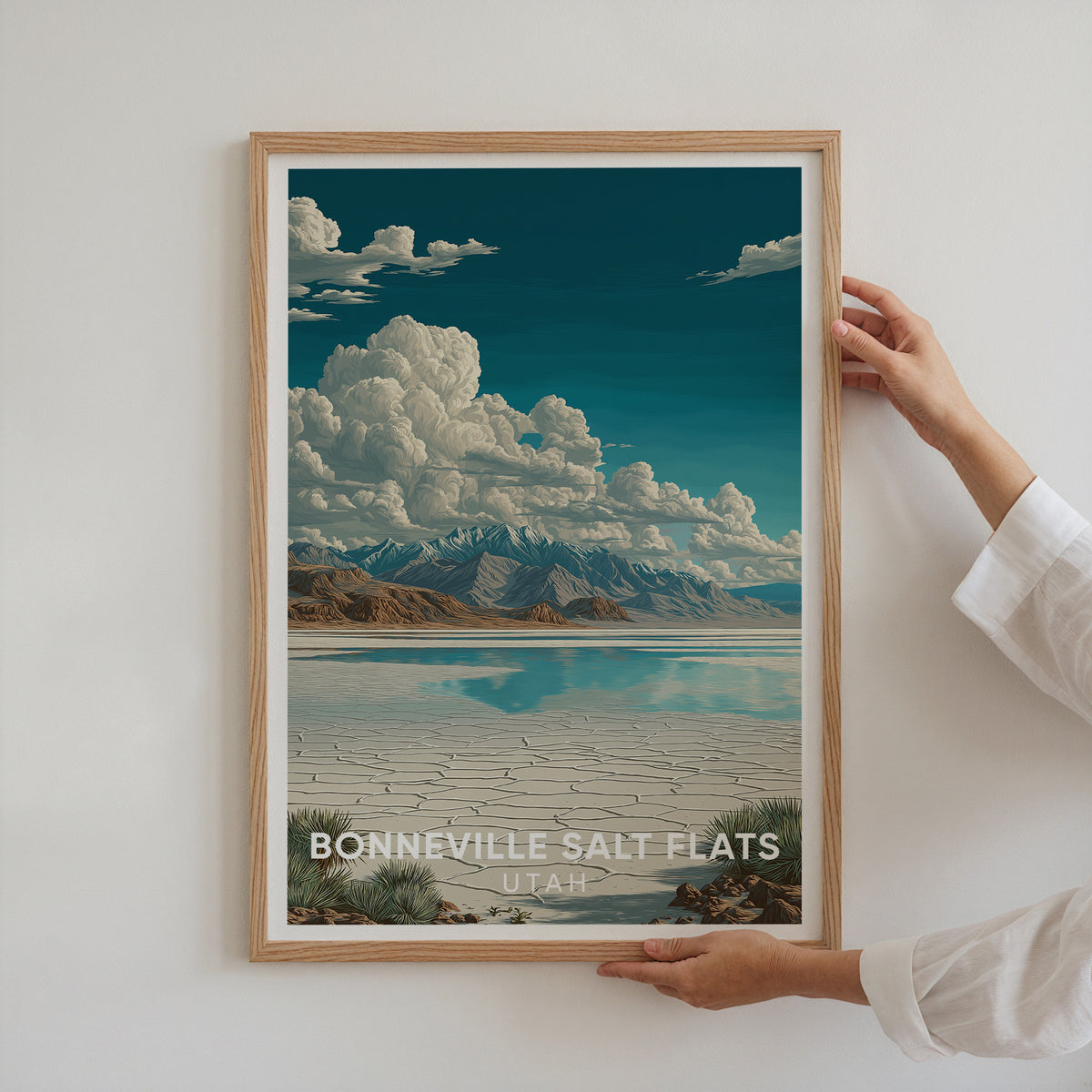 Two hands holding an oak-framed Bonneville Salt Flats print up to a white wall