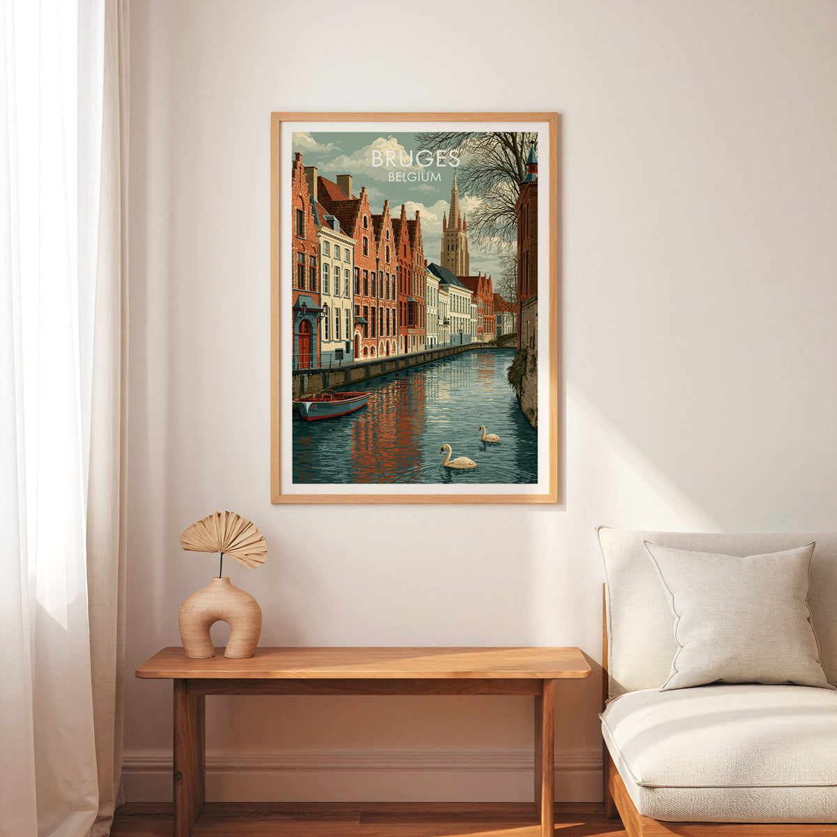 Bruges travel wall art in an oak frame above a slim wooden bench, cream armchair and a palm leaf fan in a vase