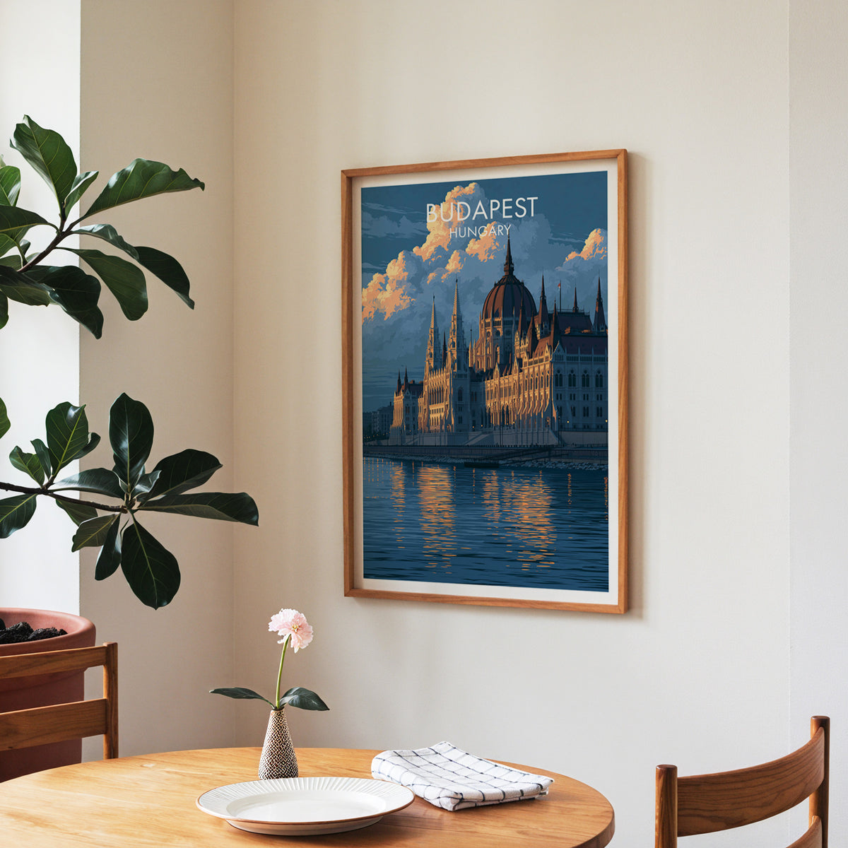 Budapest travel wall art in a walnut frame over a round dining table set with a plate, napkin and a single rose