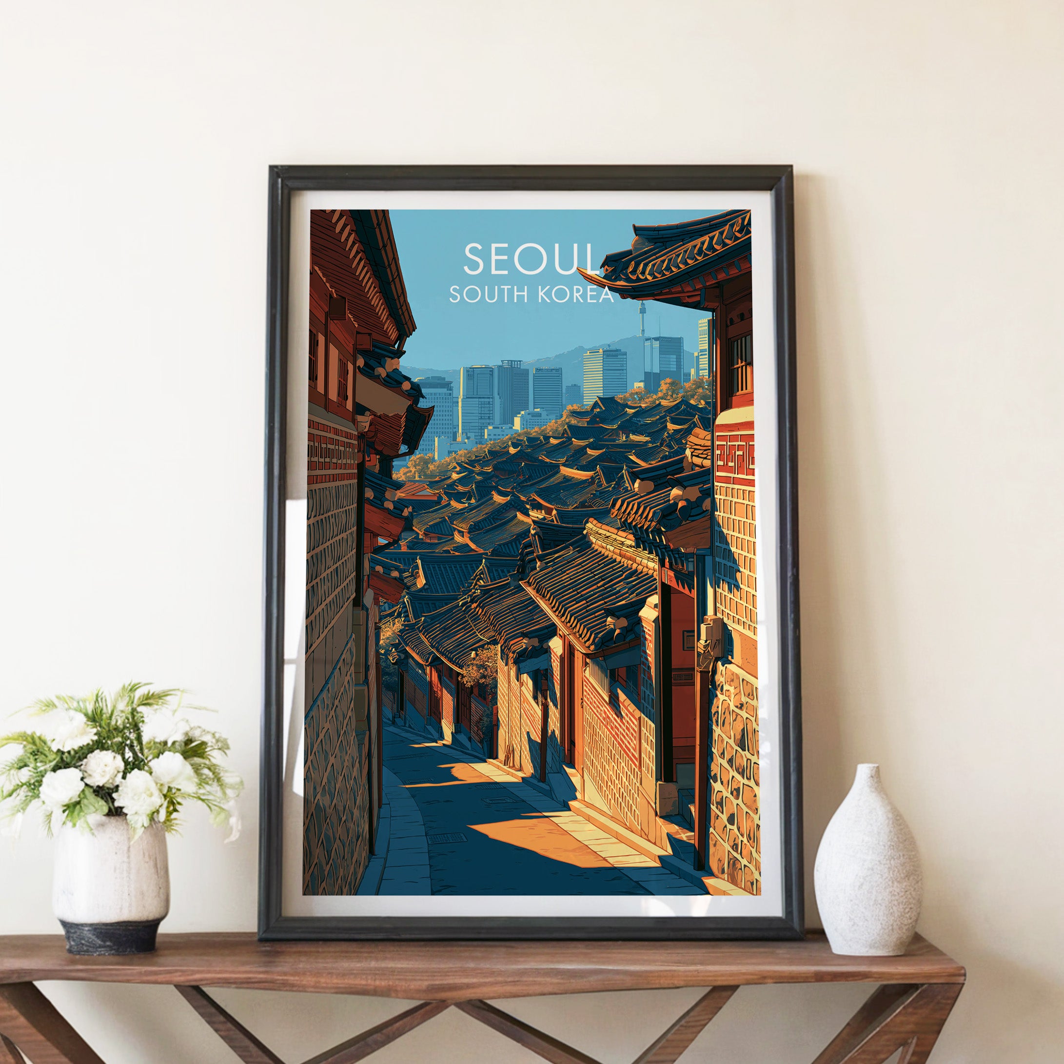 Bukchon Hanok Village Seoul travel poster in a black frame on a wooden console table with white flowers