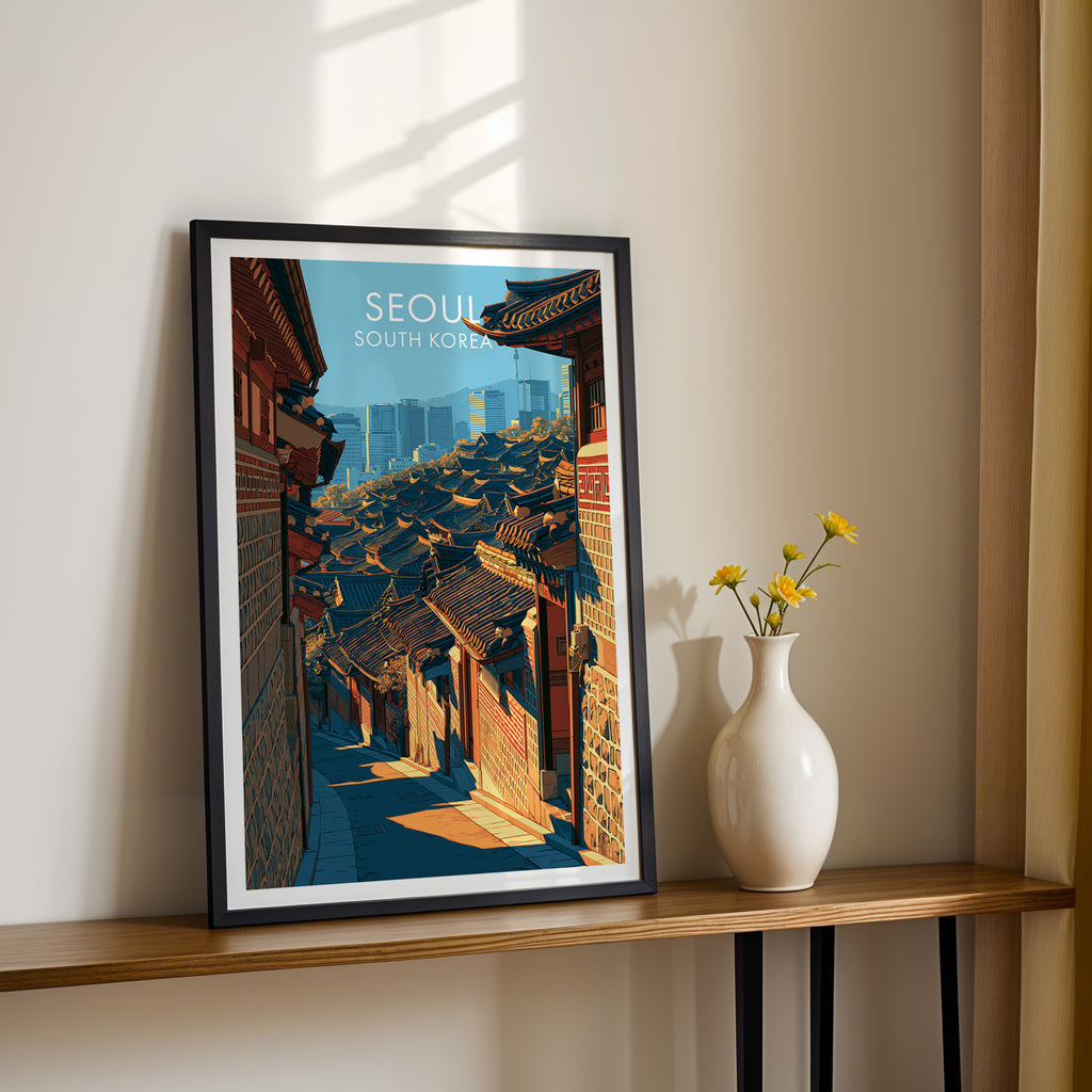 Black framed Bukchon Hanok Village Seoul print on a narrow hallway console in sunlight, styled with yellow flowers