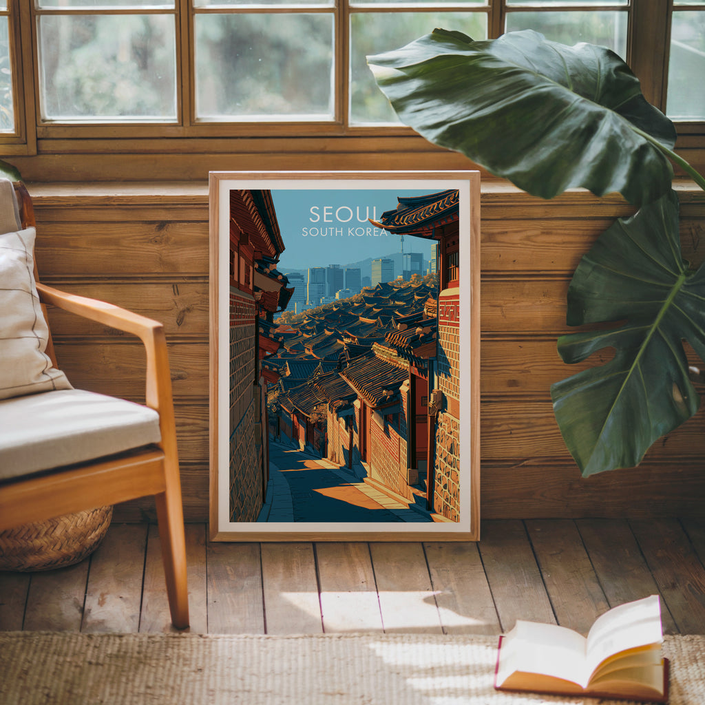 Framed Bukchon Hanok Village Seoul poster leaning against a timber cabin wall with monstera leaves and an open book