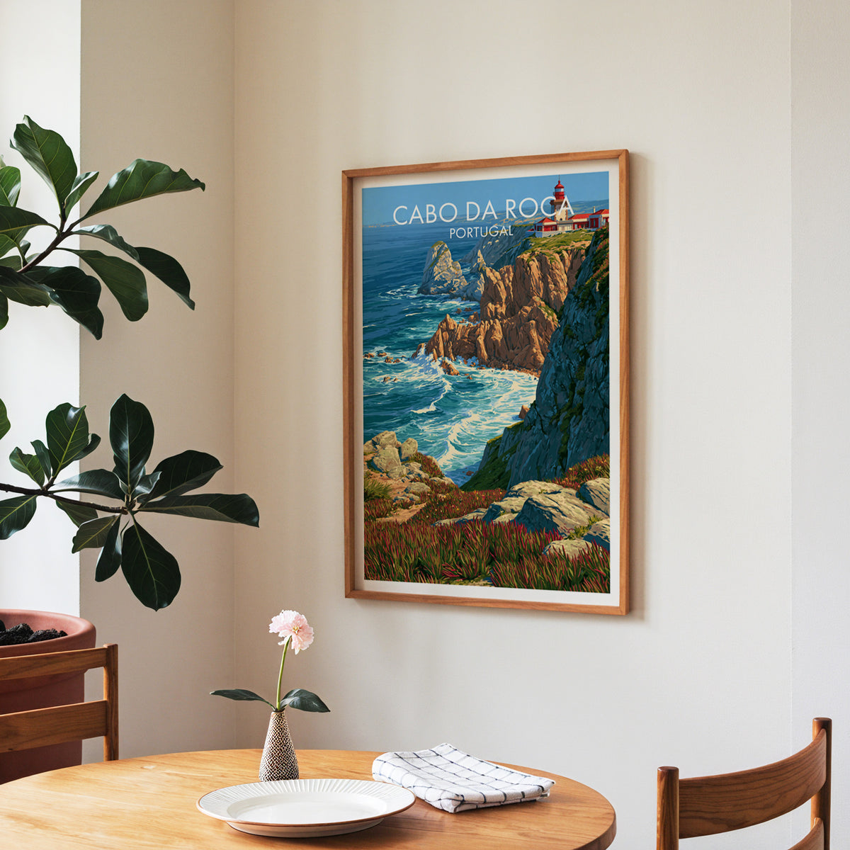 Cabo da Roca cliff surf poster, walnut frame in a dining corner above a round table and a fiddle-leaf fig