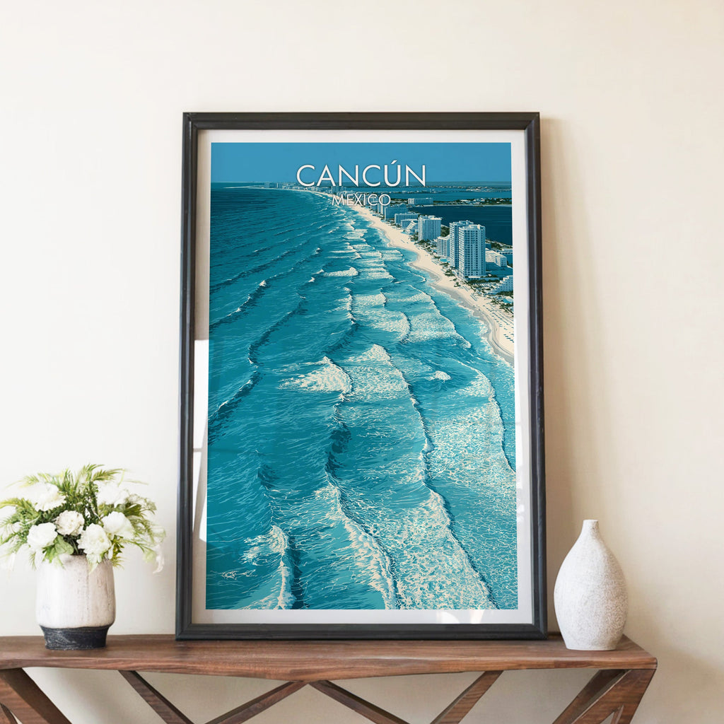 Aerial Cancun shoreline print in a black frame on a walnut console between white peonies and a ceramic vase.