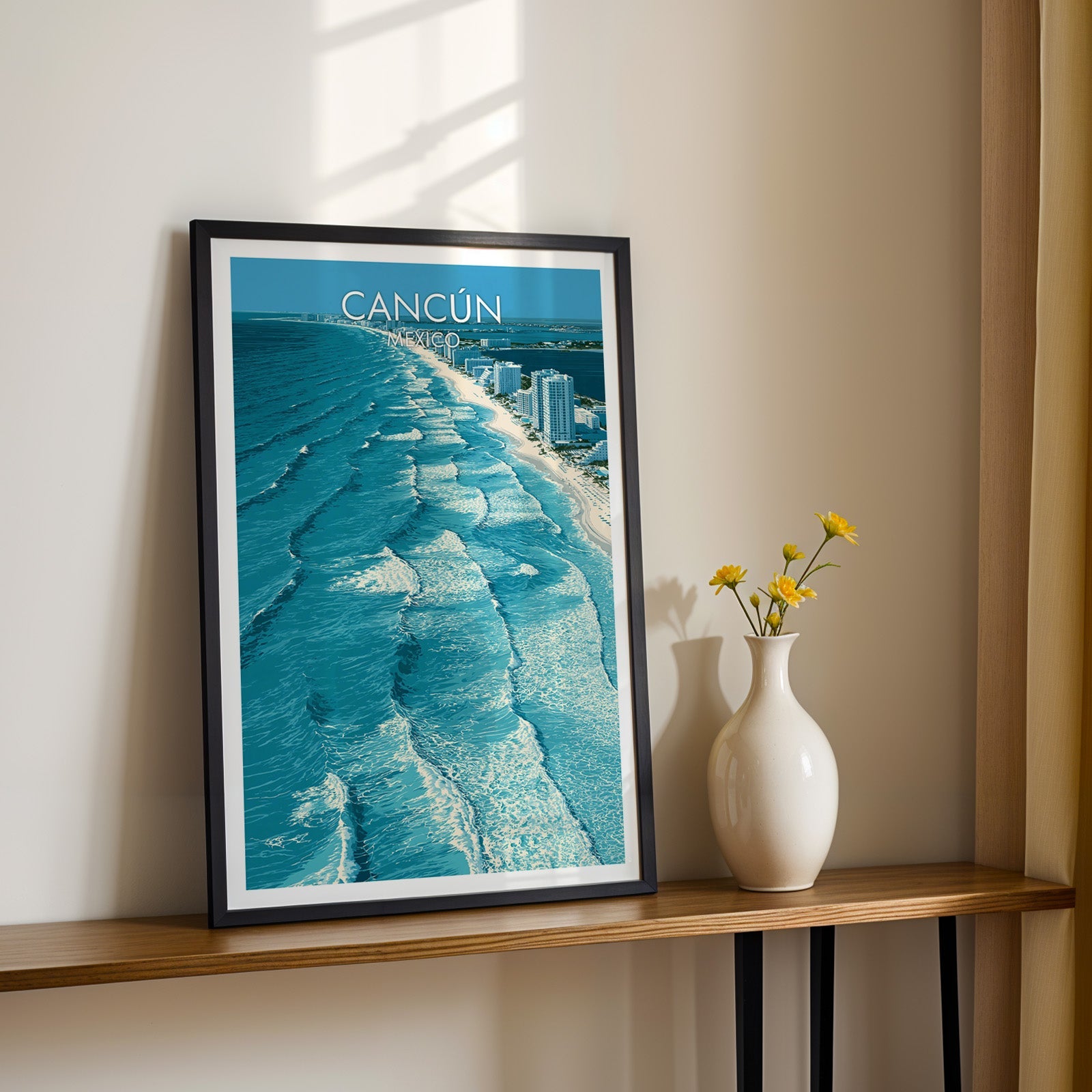 Turquoise and petrol blue wave art in a black frame on a wood shelf beside yellow daisies, sunlit cream wall.
