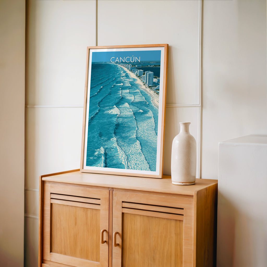 White hotel towers and teal sea, oak frame on a light oak cabinet by a cream panelled wall and bottle vase.
