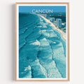 Cancun travel print of turquoise surf lines seen from above, in a light oak frame on a plain white wall.