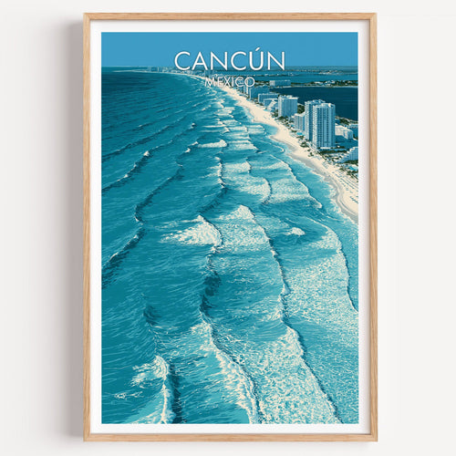 Cancun travel print of turquoise surf lines seen from above, in a light oak frame on a plain white wall.