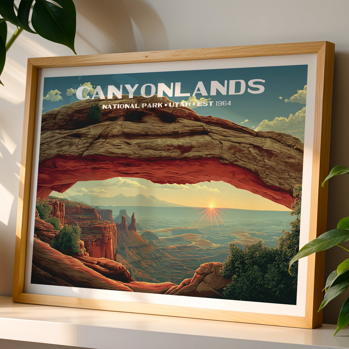 Canyonlands National Park wall art print in a light oak frame, leaning on a white shelf in warm sunlight beside a monstera plant