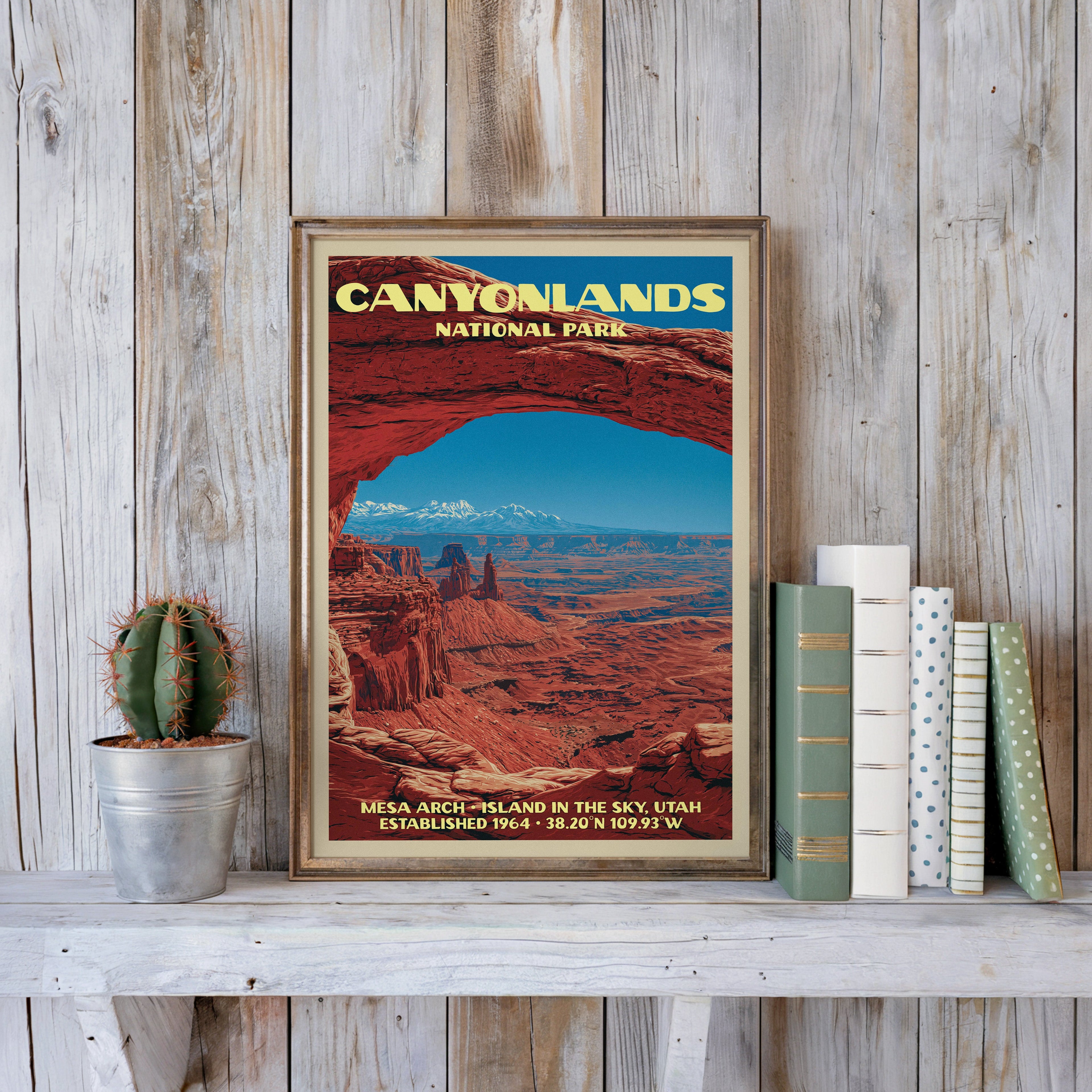 Canyonlands vintage poster in a slim gold frame on a whitewashed plank wall beside a cactus and books